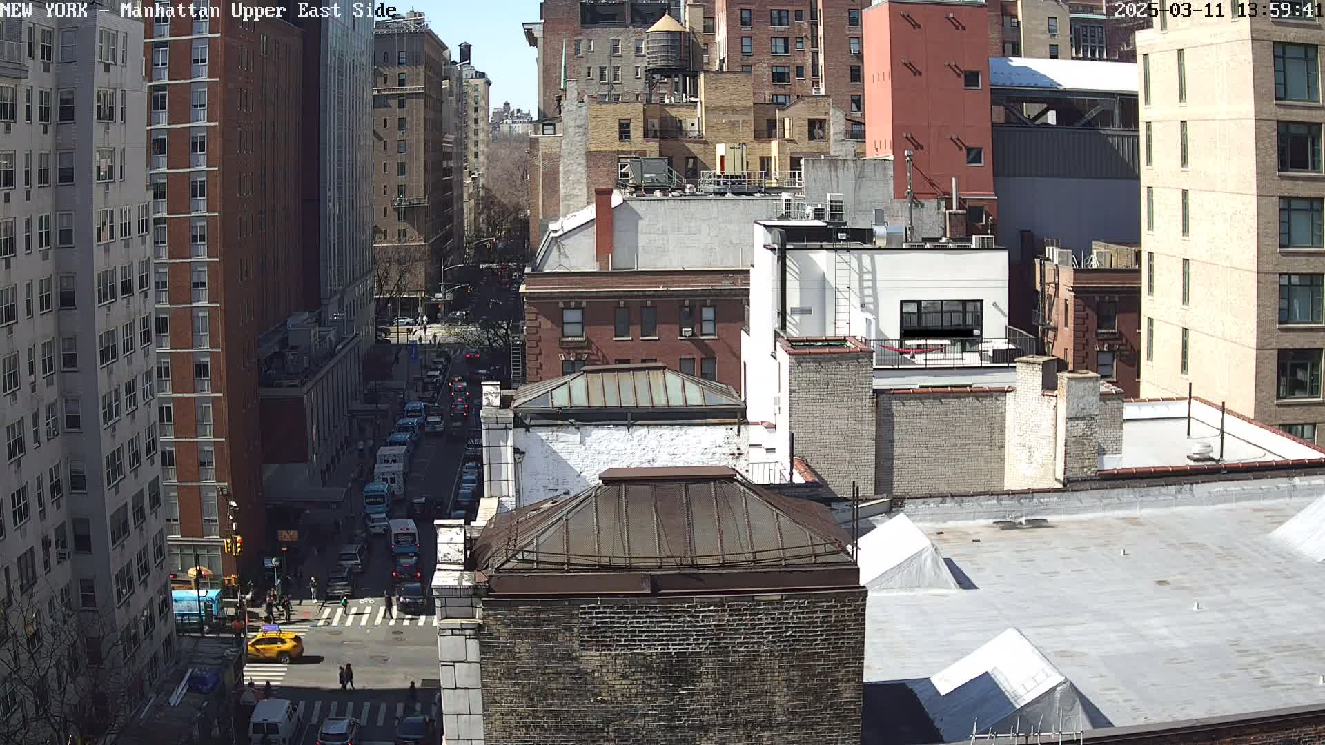 A sunny day view of a city street, showing several multi-story brick buildings and traffic on a city street below.