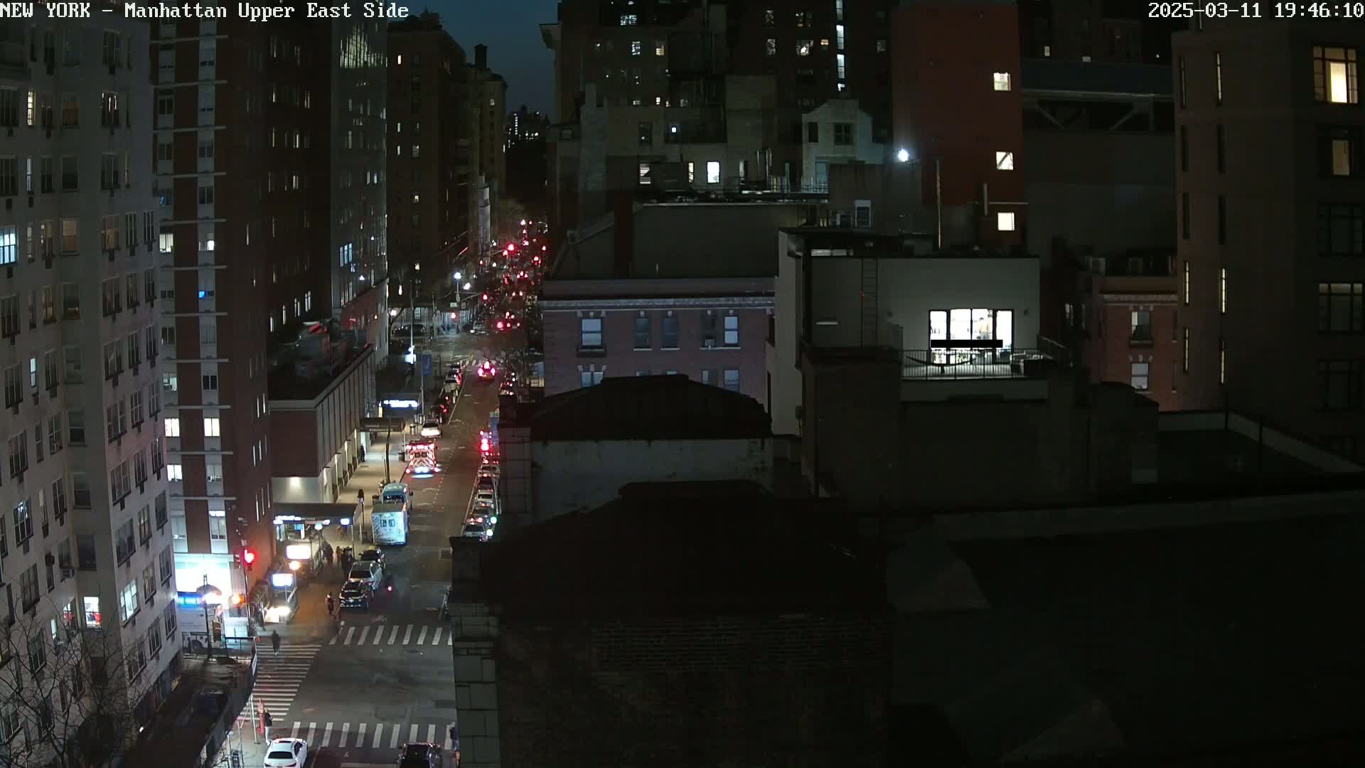 A nighttime aerial view of a city street with cars and buildings, under a dark sky.