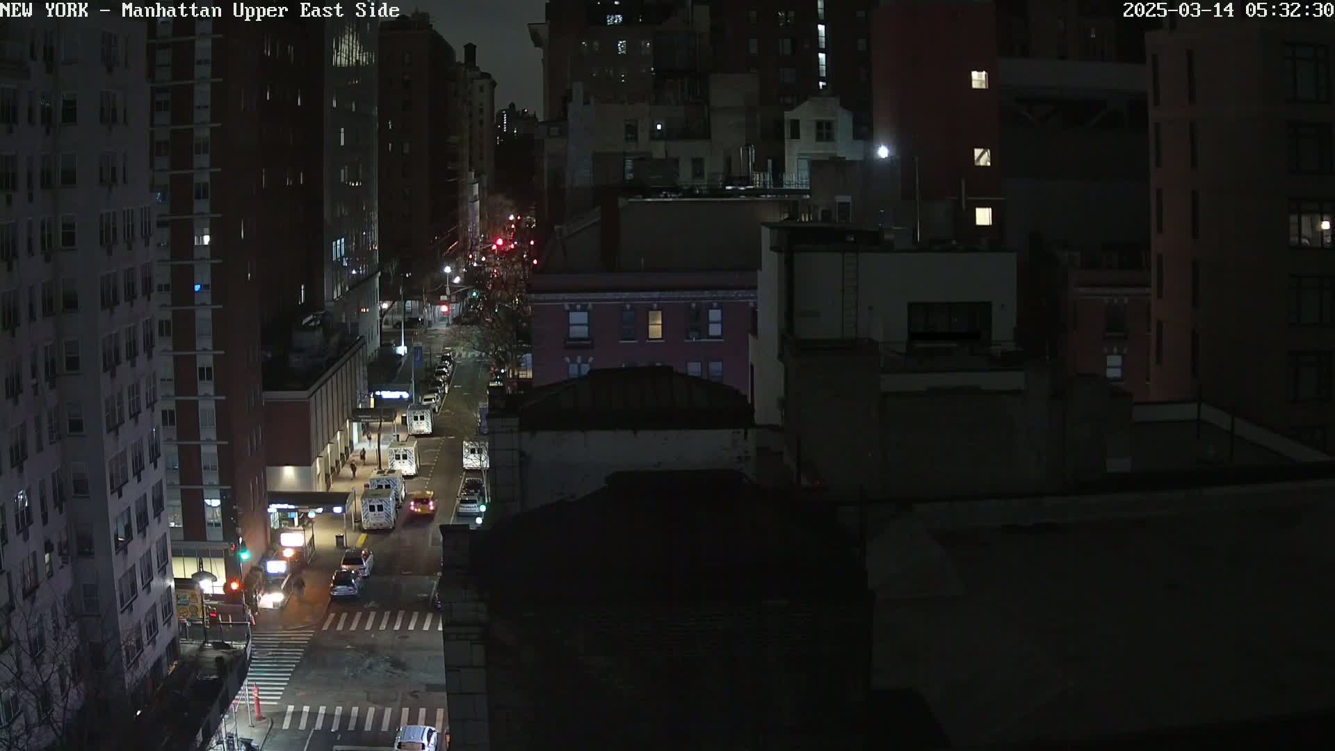 A nighttime, high-angle view of a city street with several vehicles and apartment buildings.