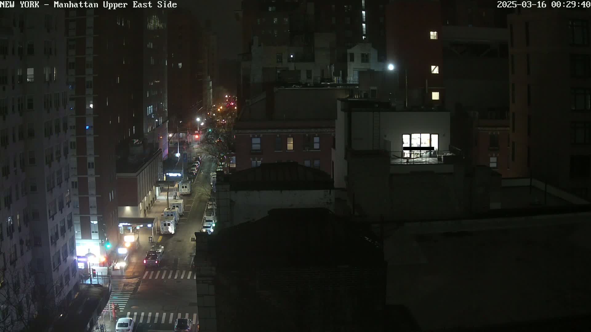 A nighttime, high-angle view of a city street with several buildings, some vehicles, and streetlights.