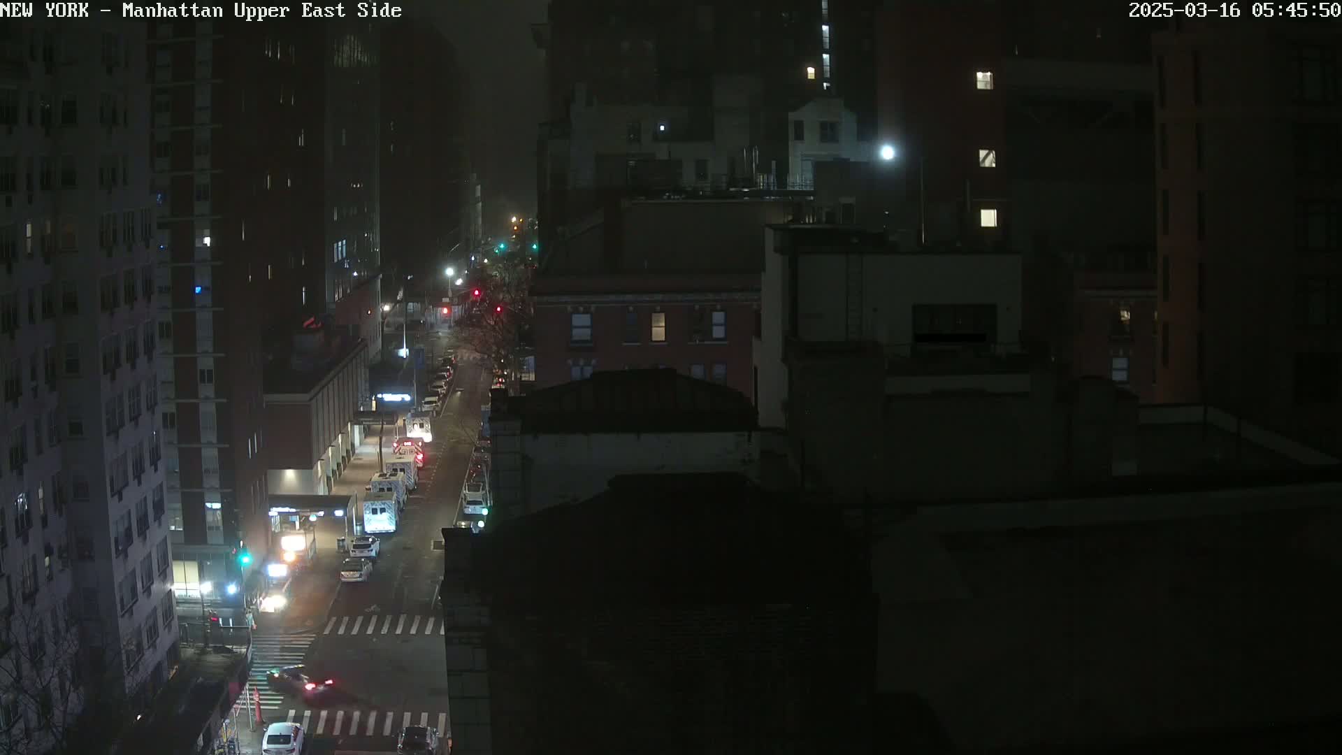 A nighttime, high-angle view of a city street with sparse traffic, showing several buildings and streetlights.