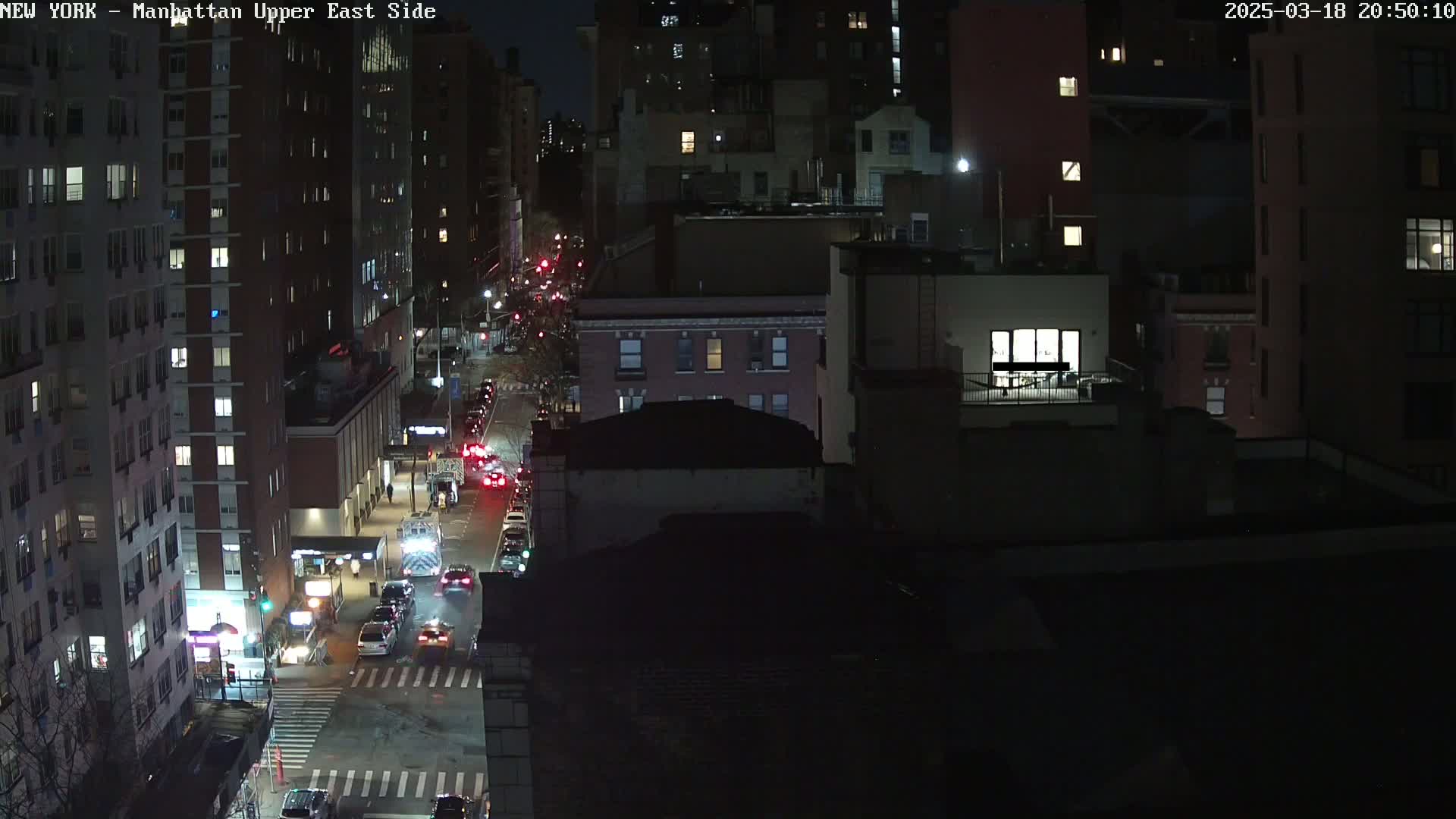 A nighttime, high-angle view of a city street with traffic and numerous apartment buildings.