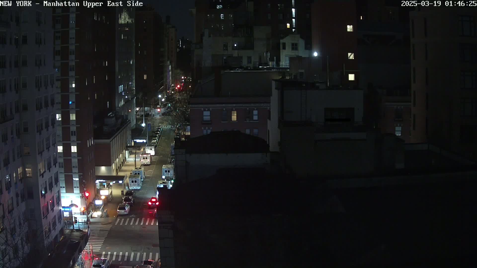 A nighttime, high-angle view of a city street with several vehicles, including what appears to be emergency vehicles, parked along the side of the road.
