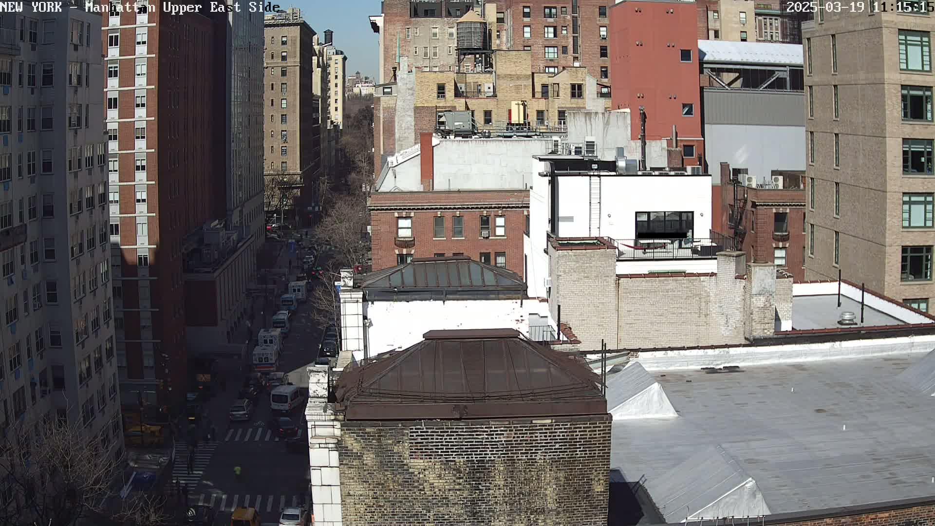 A sunny day view of a city street, showing multi-story brick buildings and vehicles on a roadway below.