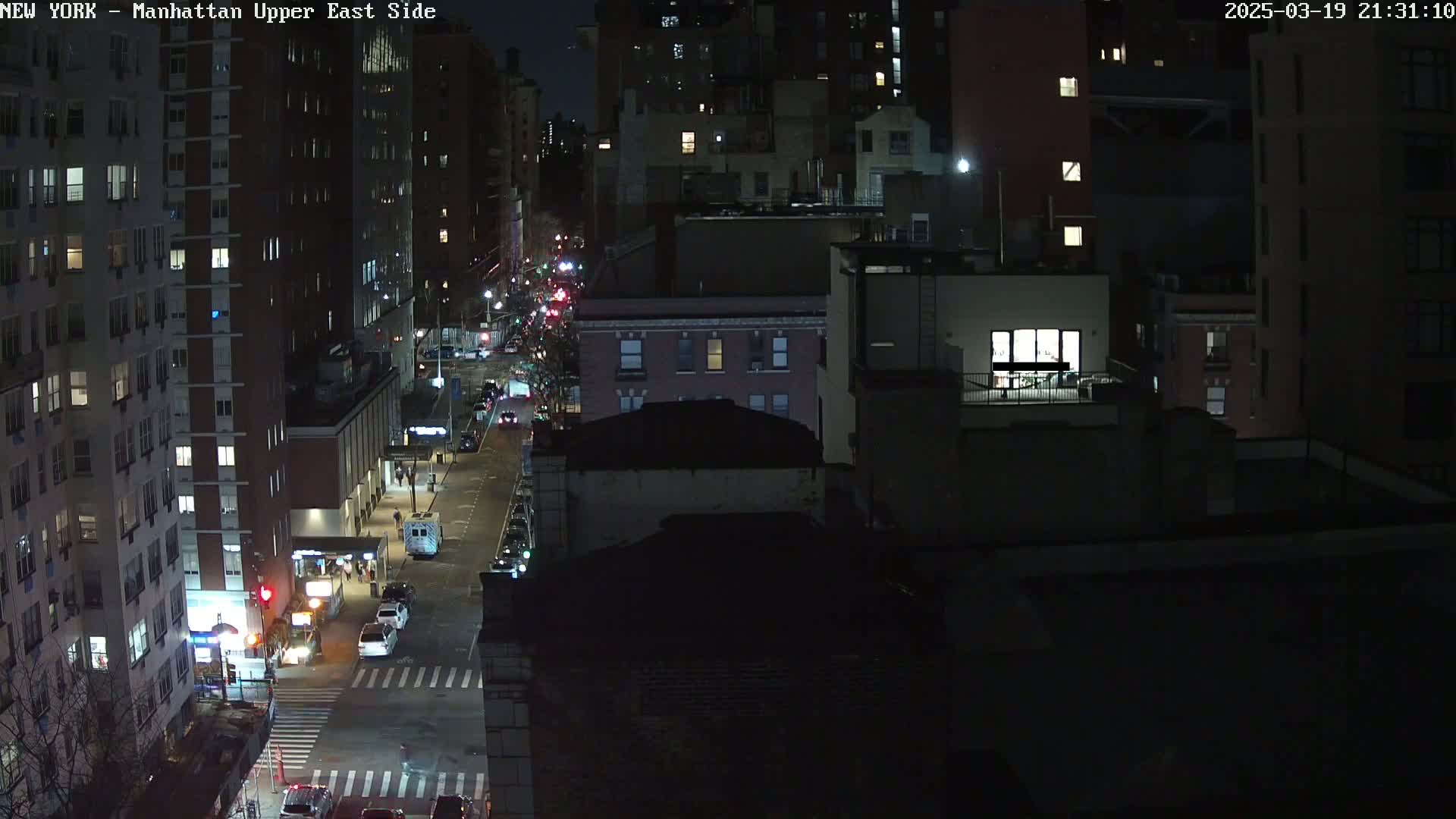 A nighttime, high-angle view of a city street with sparsely trafficked vehicles and tall buildings.