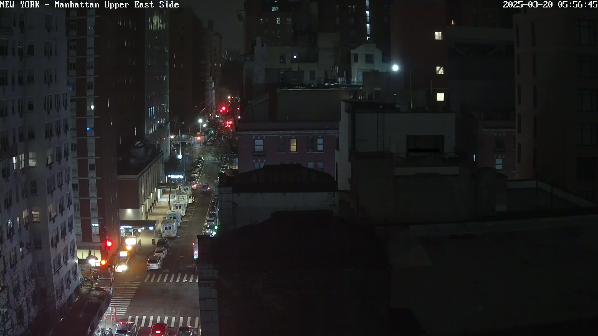 A nighttime, high-angle view of a city street with several vehicles and buildings under dark, clear skies.