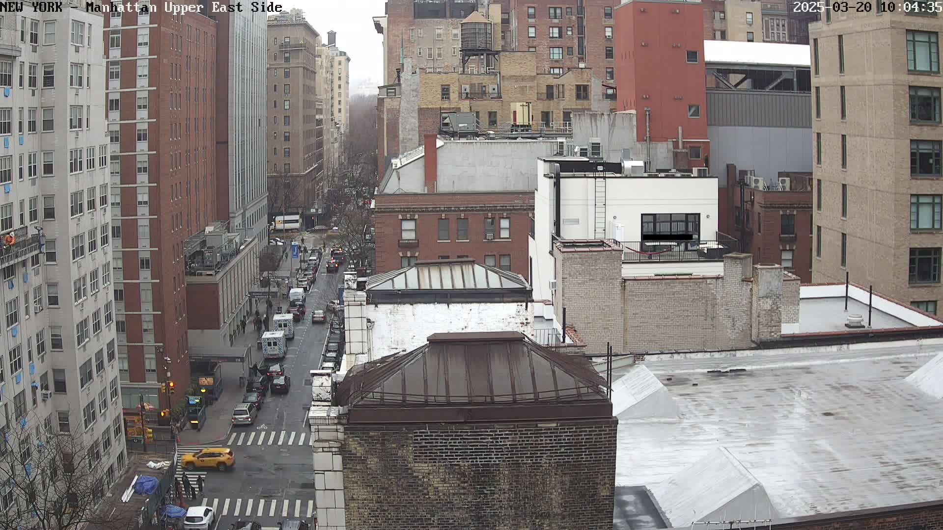 A high-angle view of city buildings on an overcast day, showing a street with cars and a few pedestrians.