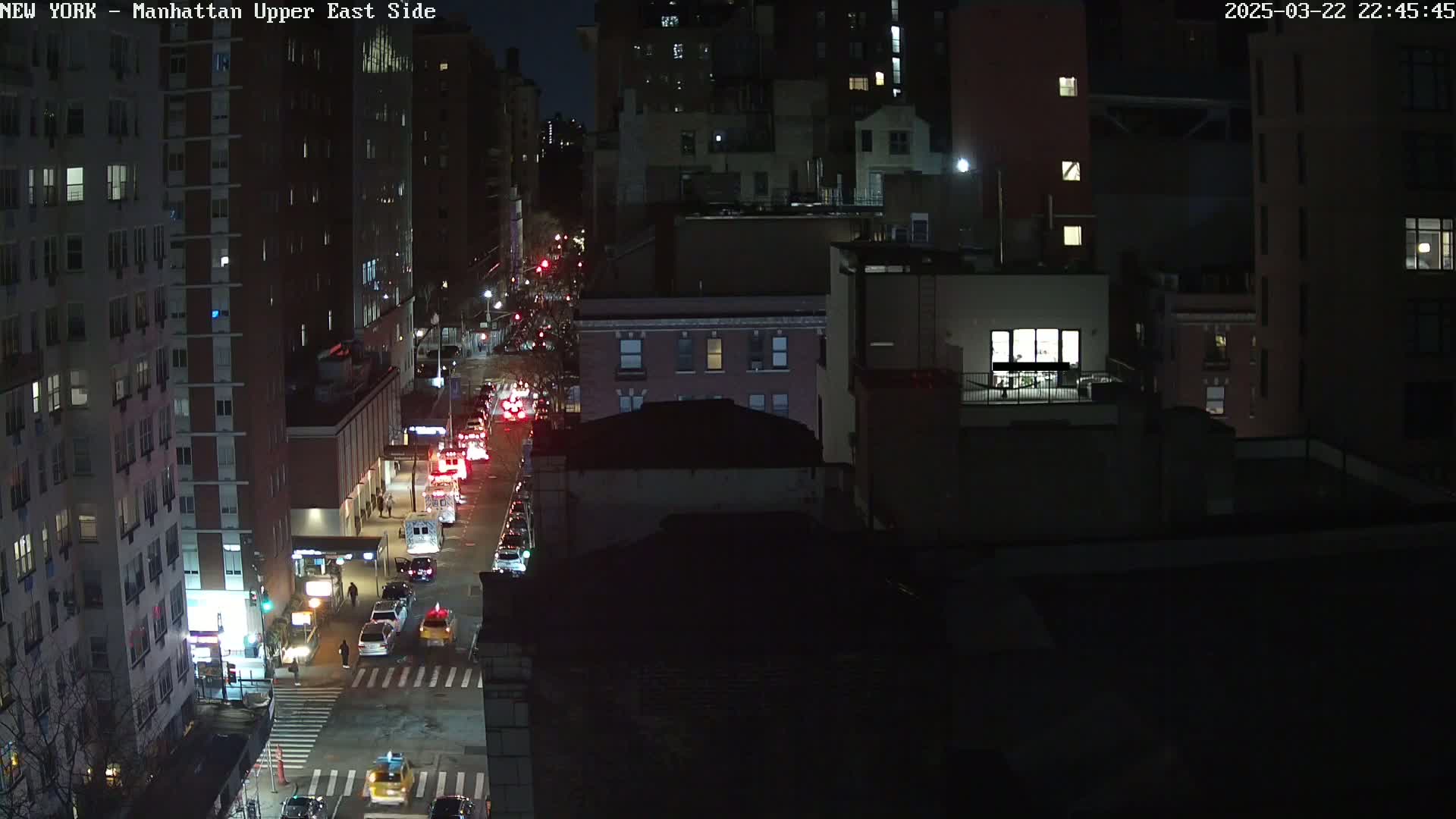 A nighttime, high-angle view of a city street with traffic moving in both directions, surrounded by tall buildings.