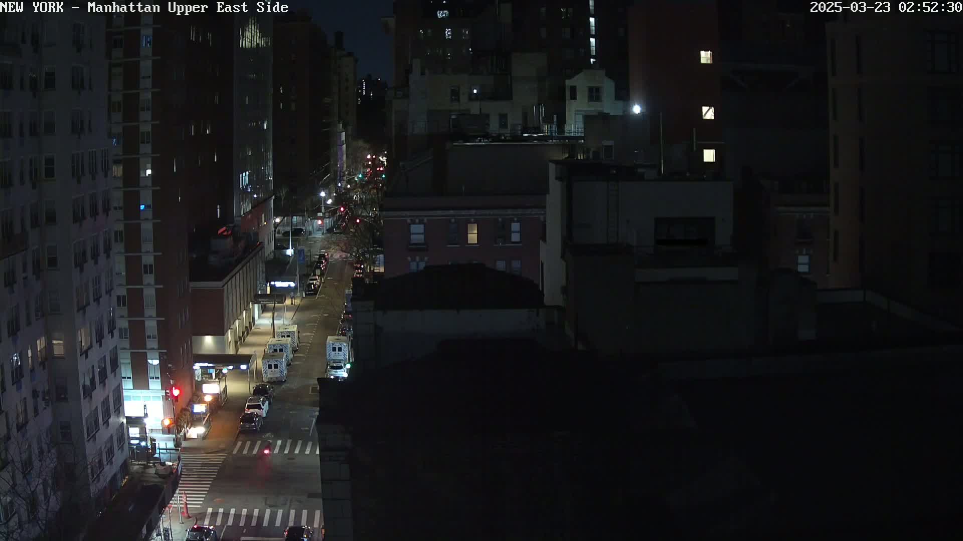 A nighttime, high-angle view shows a city street with several cars and buildings under dark, clear skies.