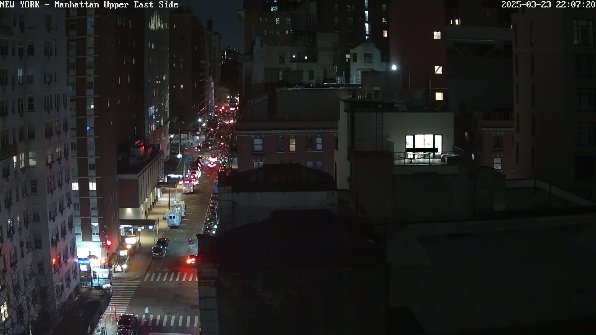A nighttime aerial view of a city street with cars driving on it, surrounded by tall buildings.