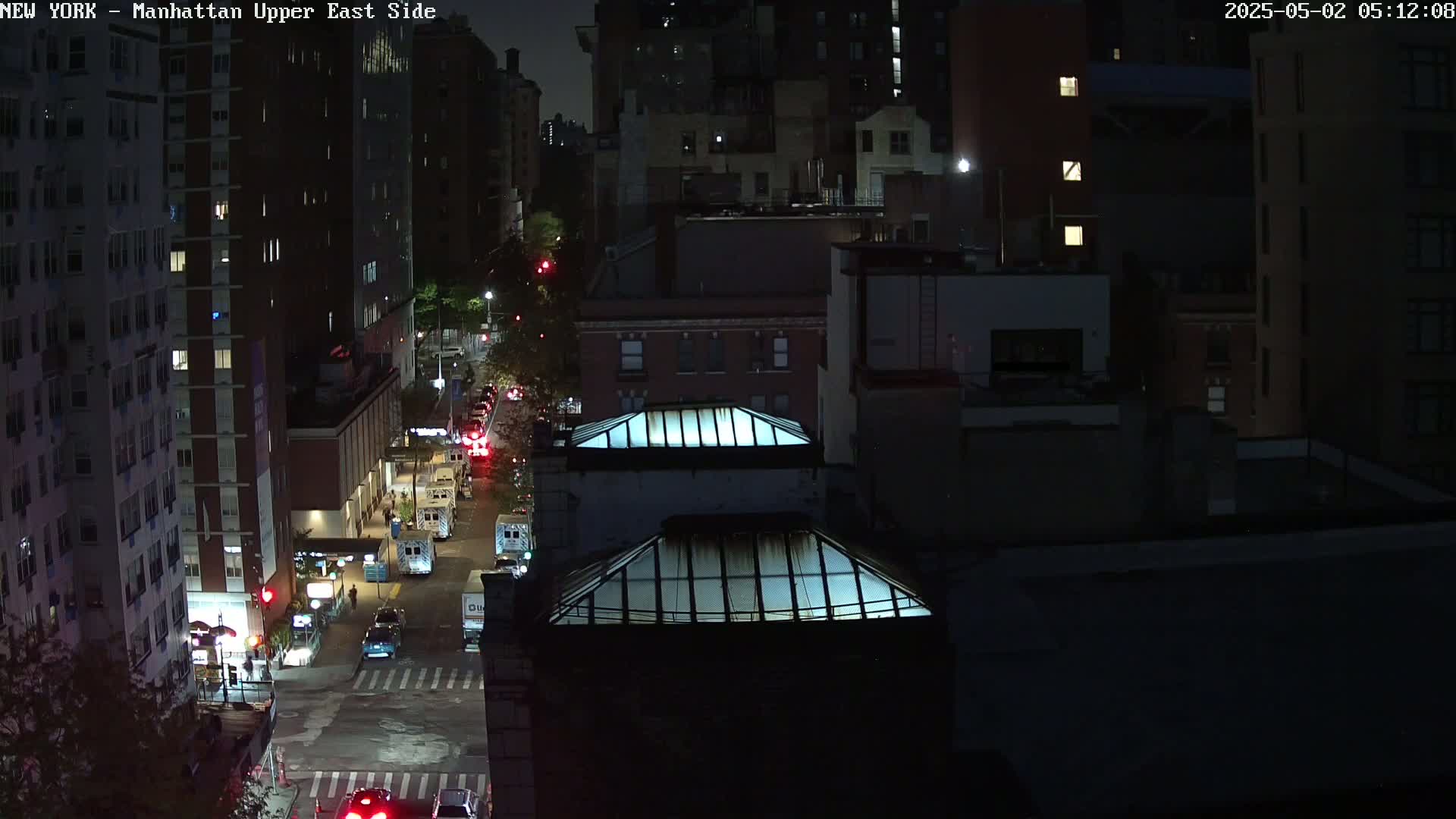 A nighttime aerial view of a city street with several buildings and vehicles, illuminated by streetlights.