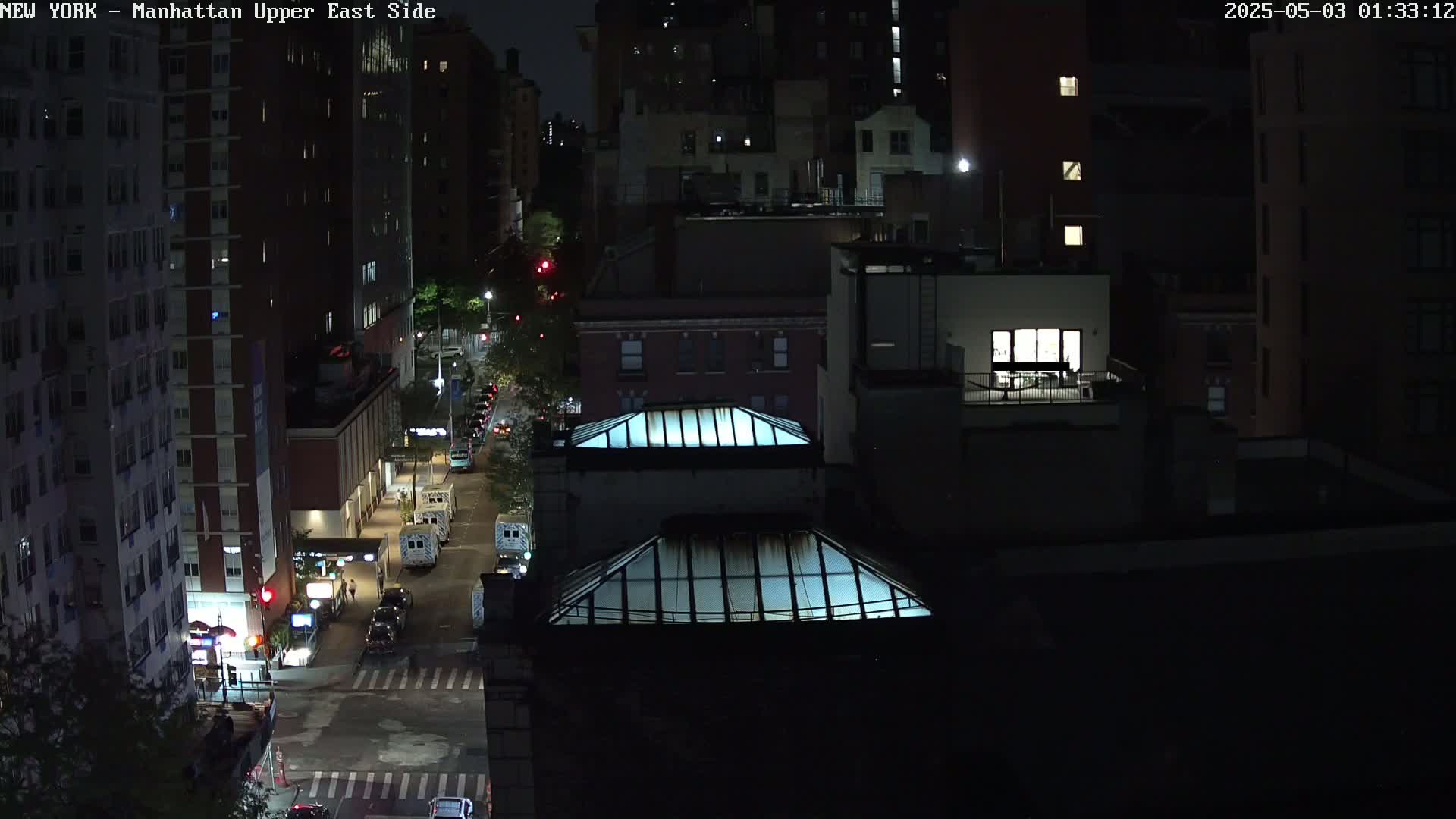A nighttime aerial view of a city street shows several buildings and vehicles, illuminated by streetlights.