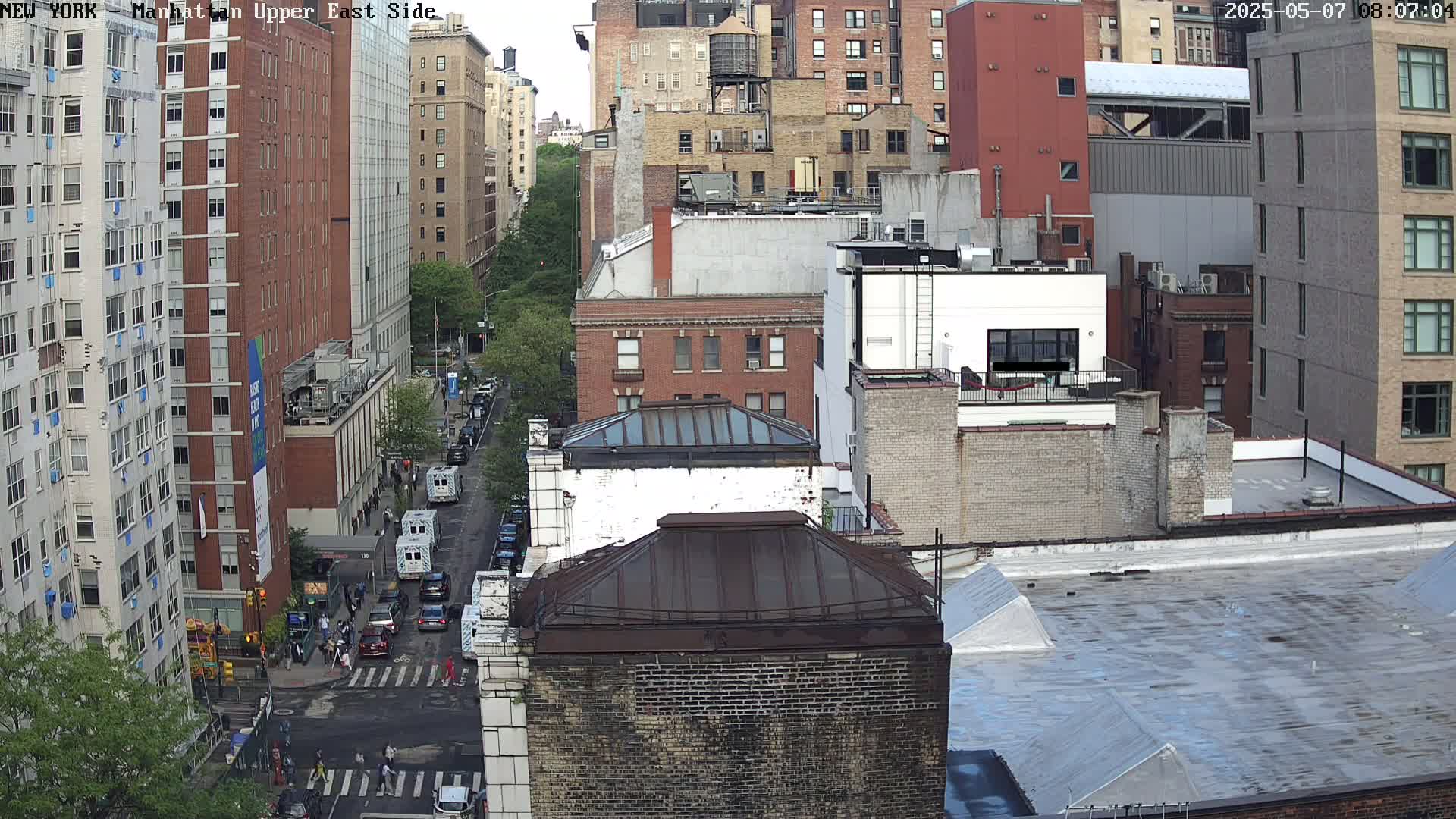 An aerial view of a city street shows several multi-story brick buildings under an overcast sky.