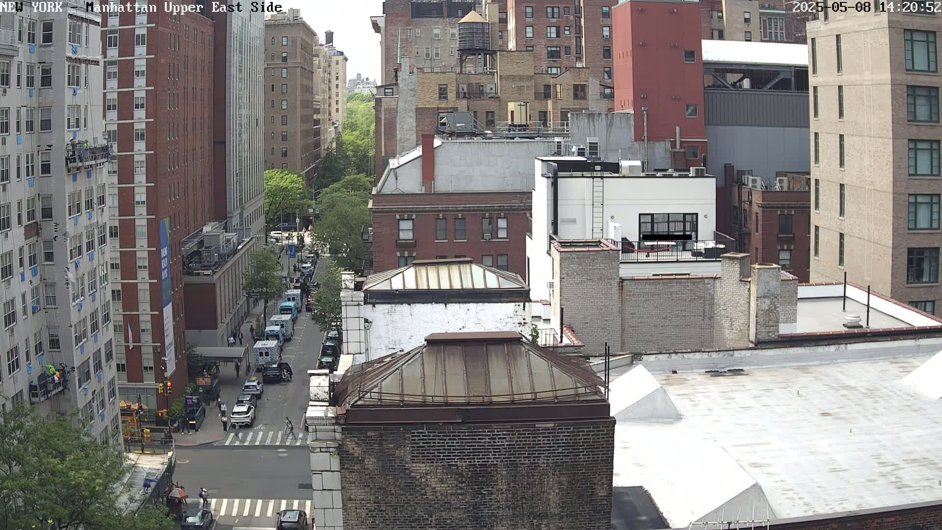 A high-angle view of a city street shows several multi-story buildings on a partly sunny day.