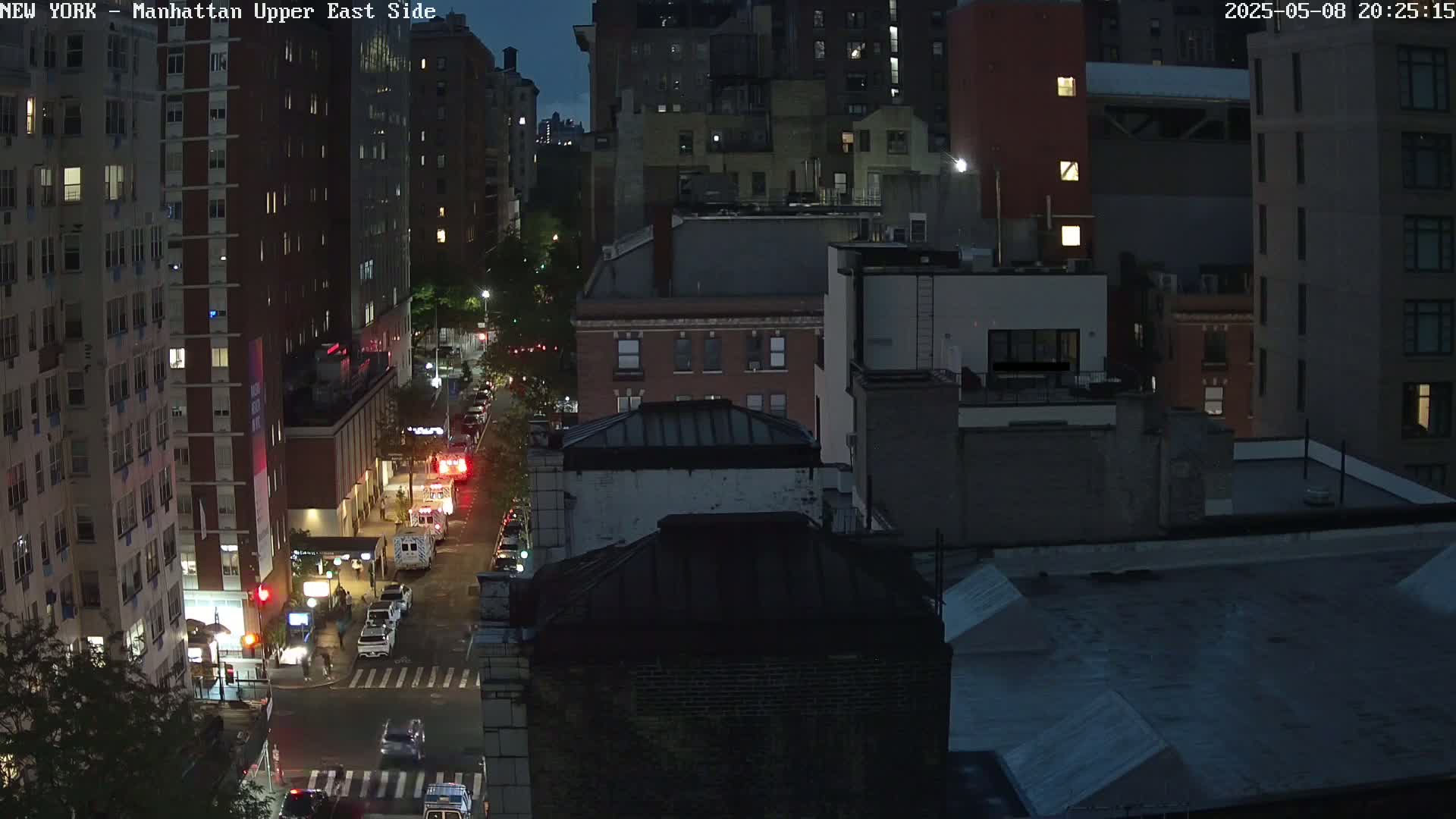 A nighttime aerial view of a city street, showing several multi-story buildings and emergency vehicles parked along a road.