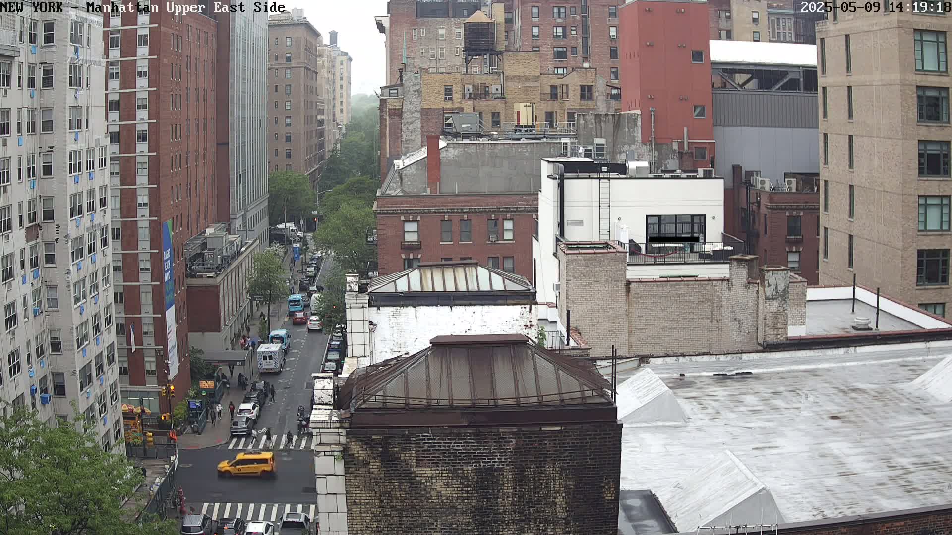 A high-angle, long shot of a city street on an overcast day, showing several multi-story brick buildings and vehicles on the street below.