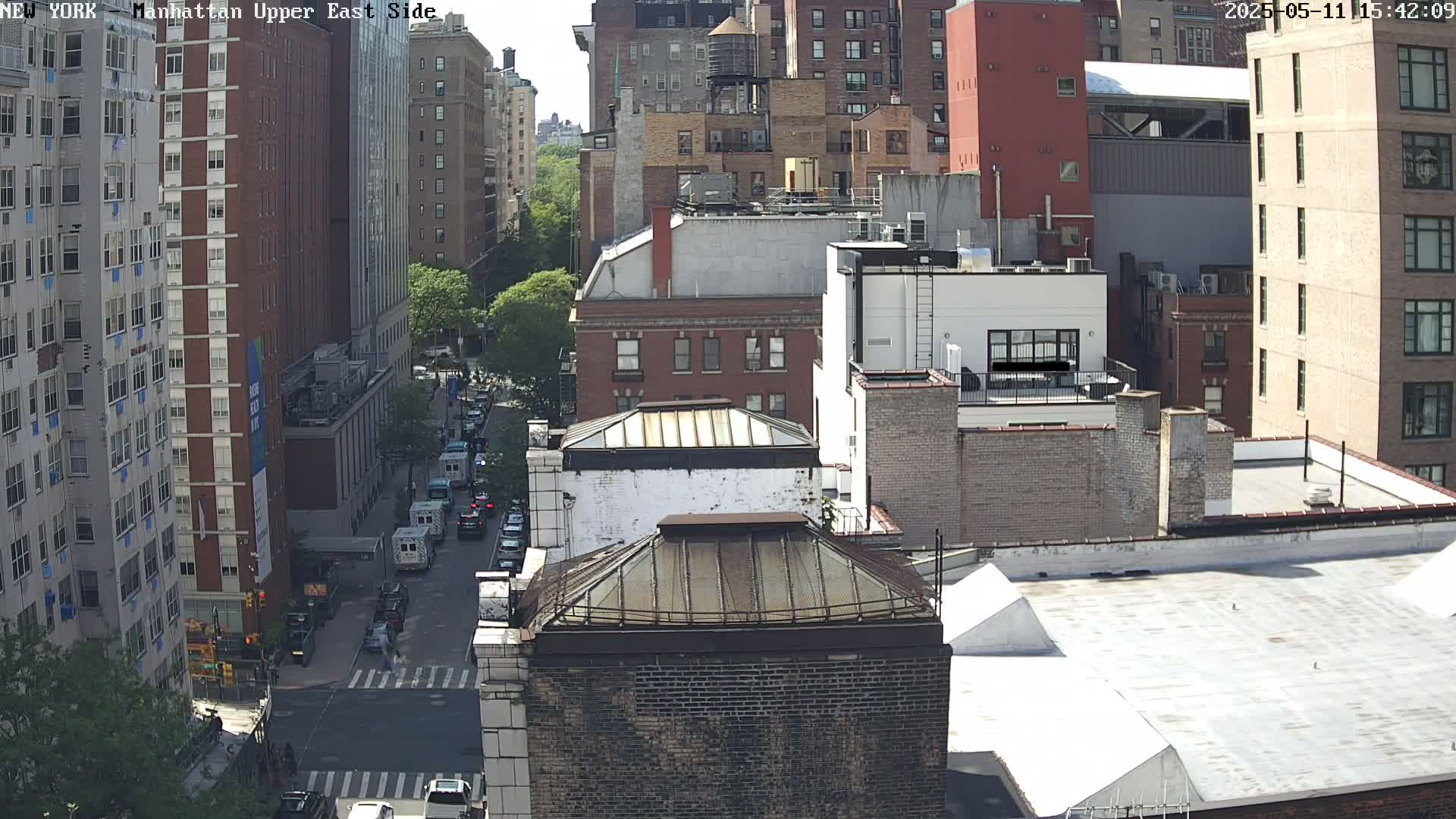 A high-angle view of a city street scene on a sunny day, showing several multi-story brick buildings and a few cars on the street below.