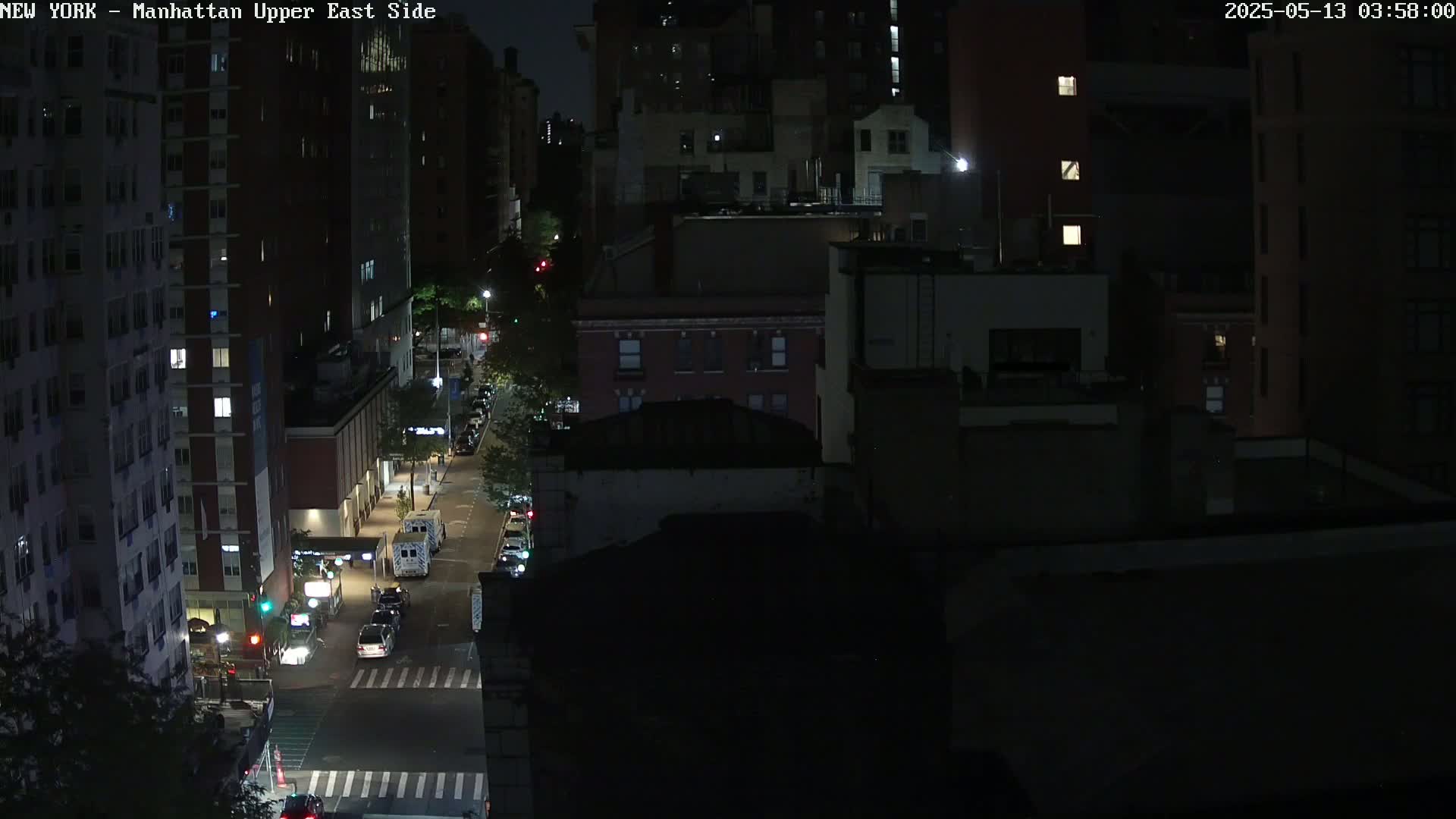 A nighttime, high-angle view shows a city street with several vehicles and buildings under dark skies.