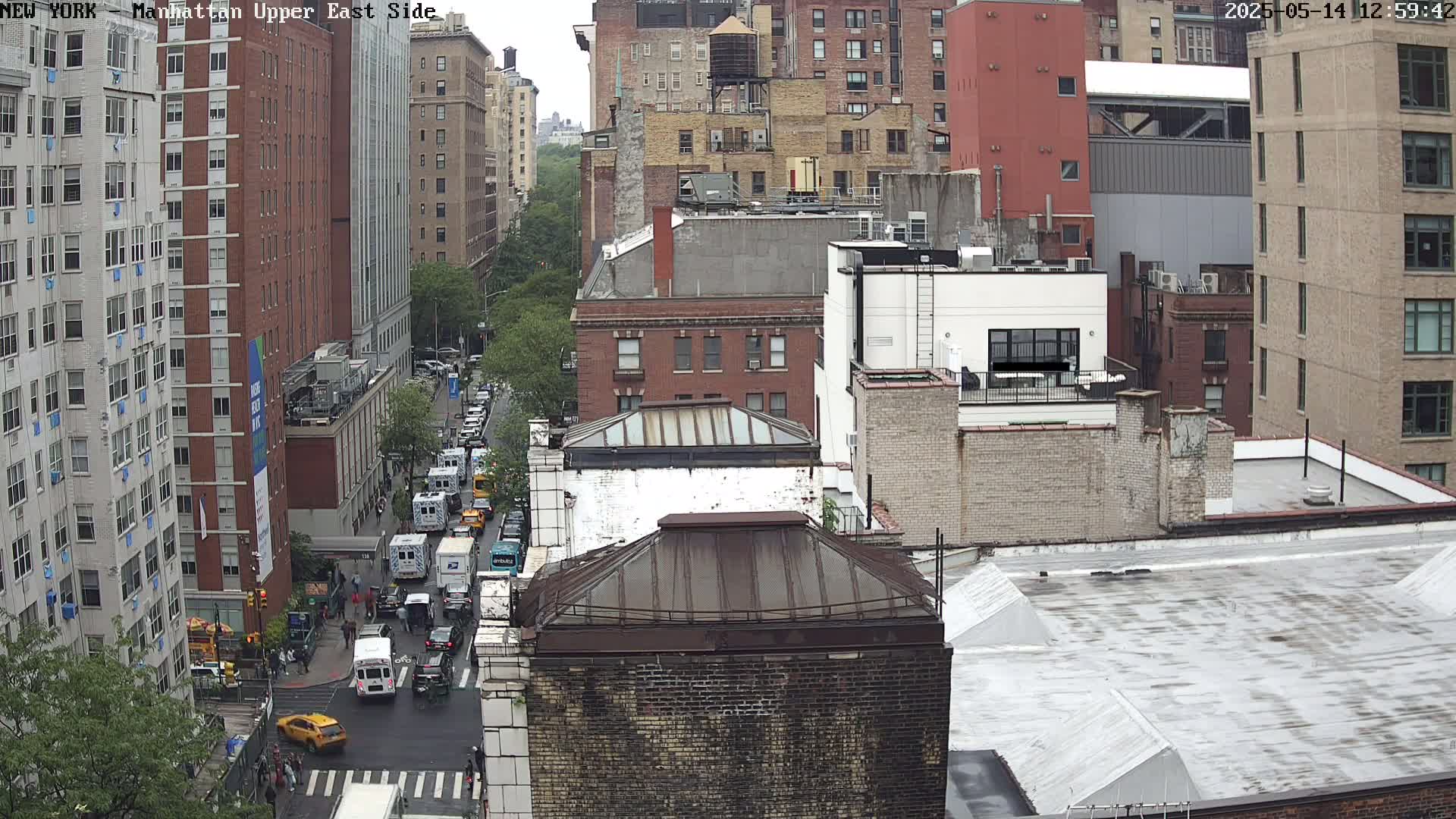 An overcast day reveals a city street scene with numerous brick buildings and vehicles, viewed from a high vantage point.