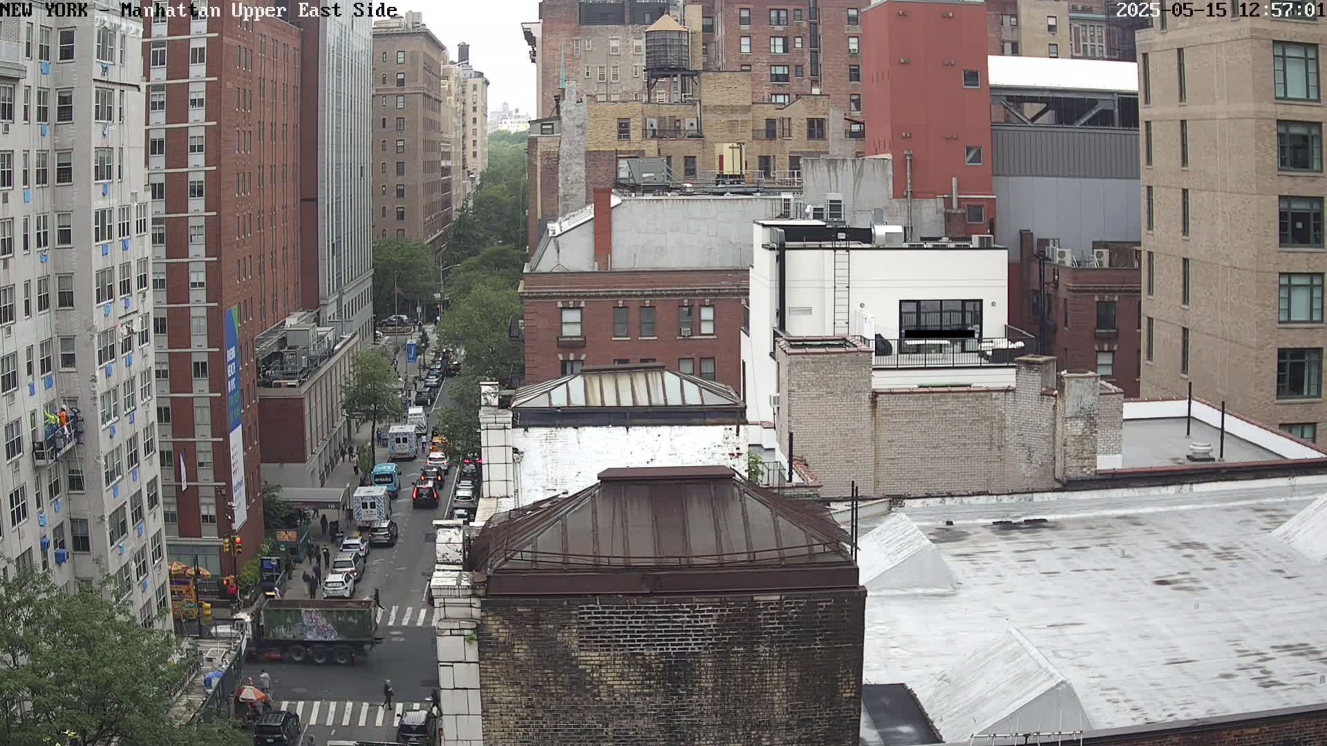 A high-angle view of a city street with numerous buildings, some under construction, on an overcast day.