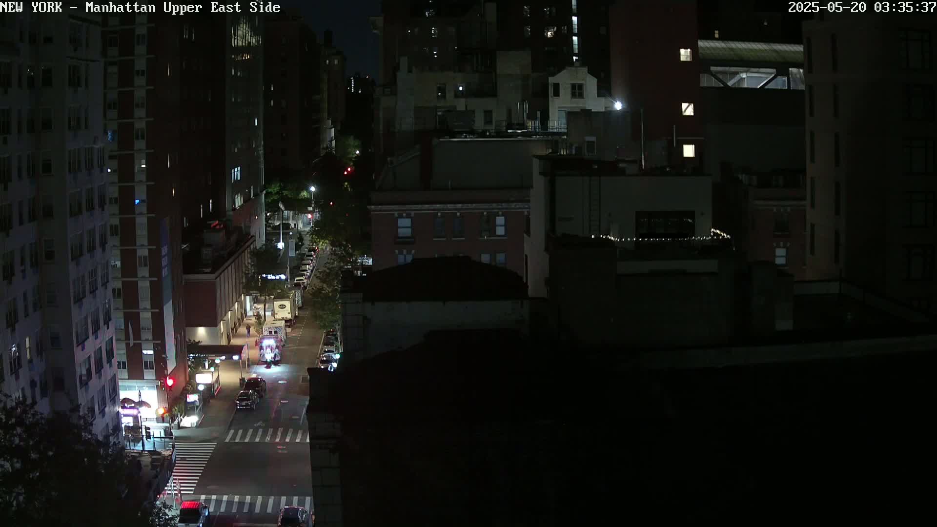 A nighttime, high-angle view shows a city street with several vehicles, bordered by dark multi-story buildings under a clear sky.