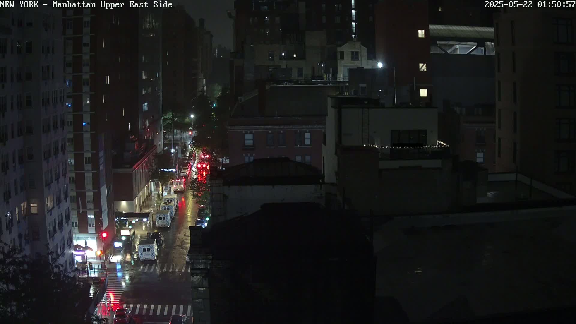 A nighttime, rain-slicked city street scene shows several vehicles and tall buildings under dim streetlights.