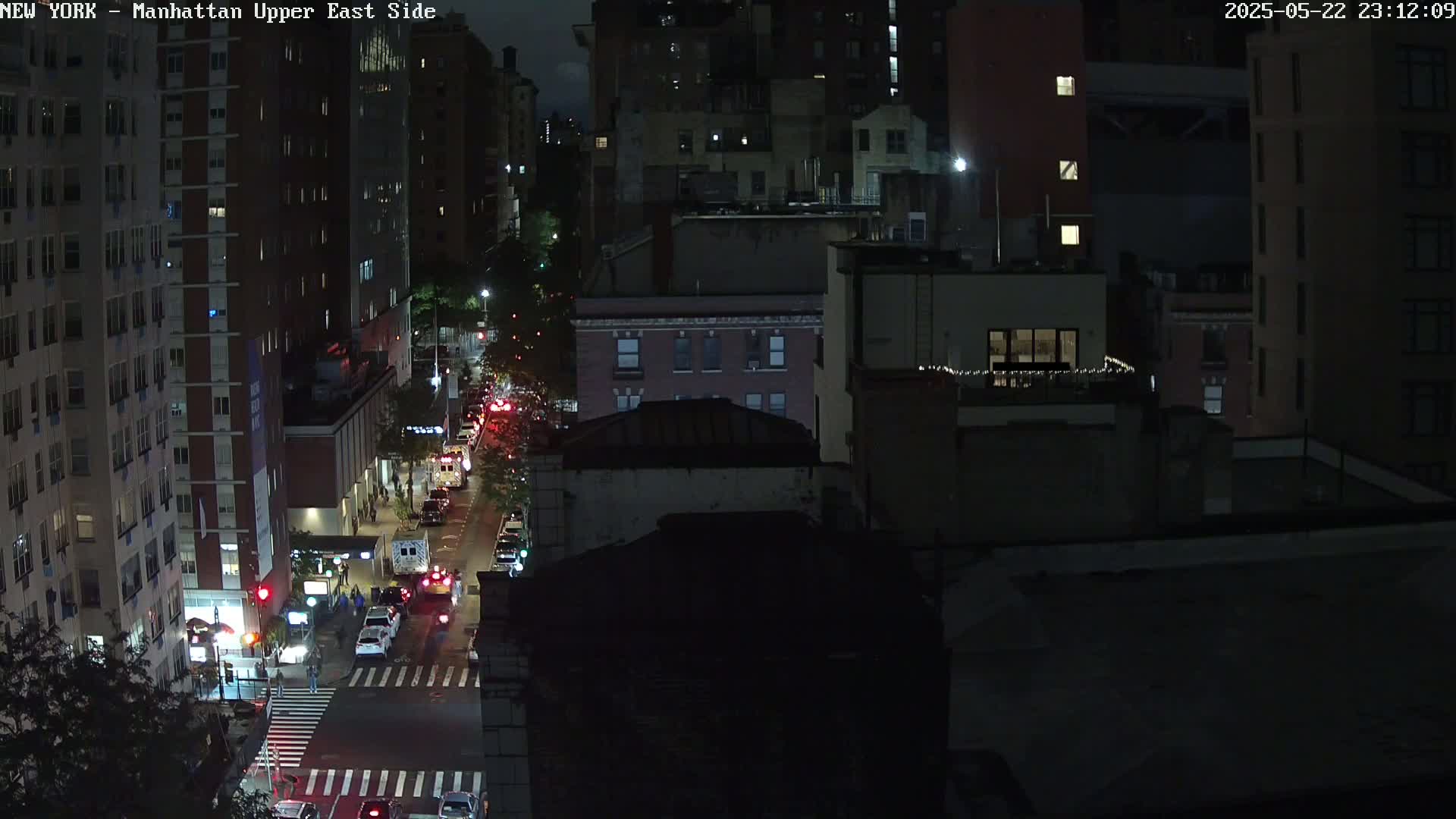 A nighttime, high-angle view of a city street with cars driving on it, surrounded by dark buildings.