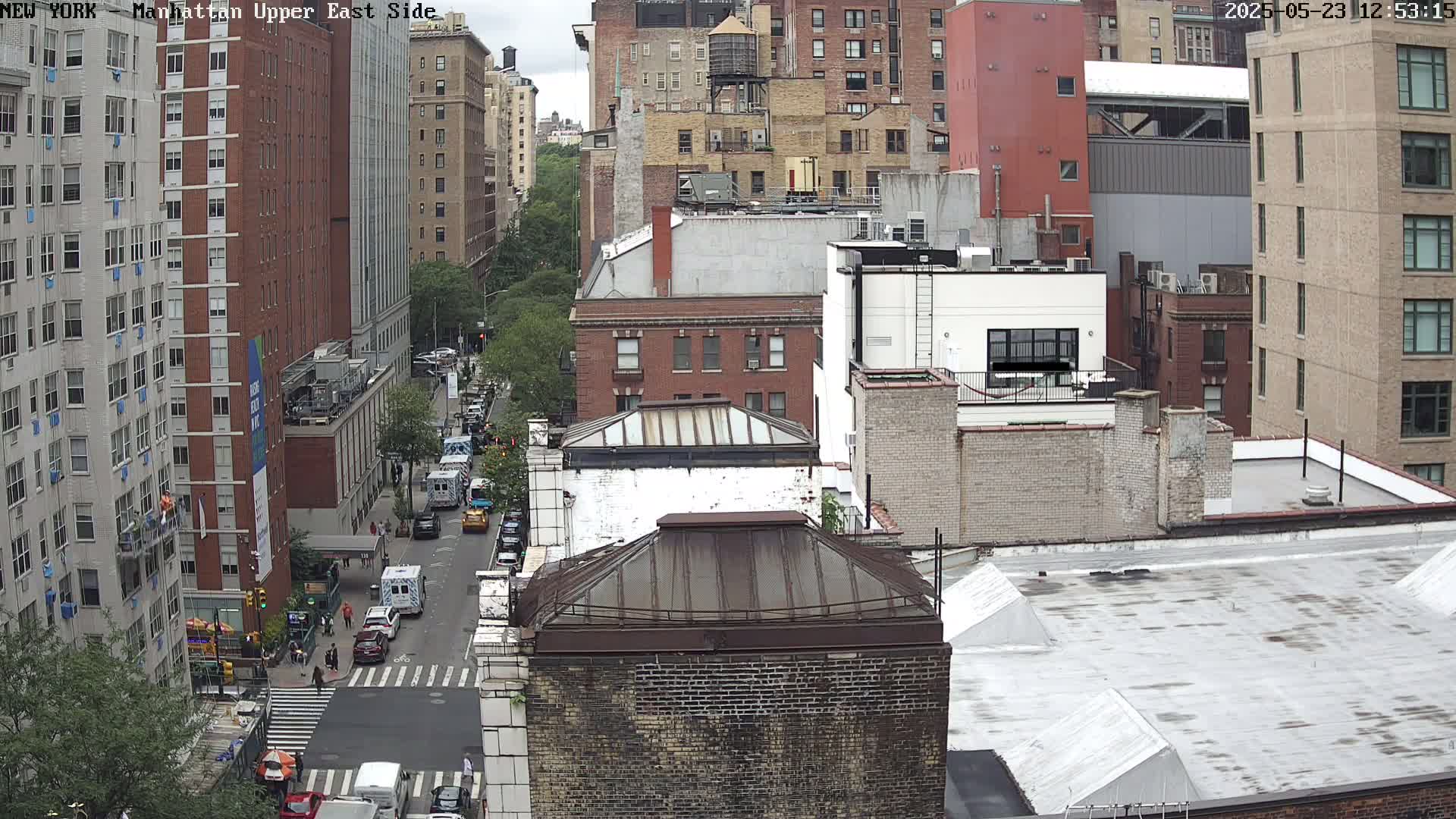 A high-angle view of city buildings on a partly cloudy day, showing a street with cars and pedestrians below.