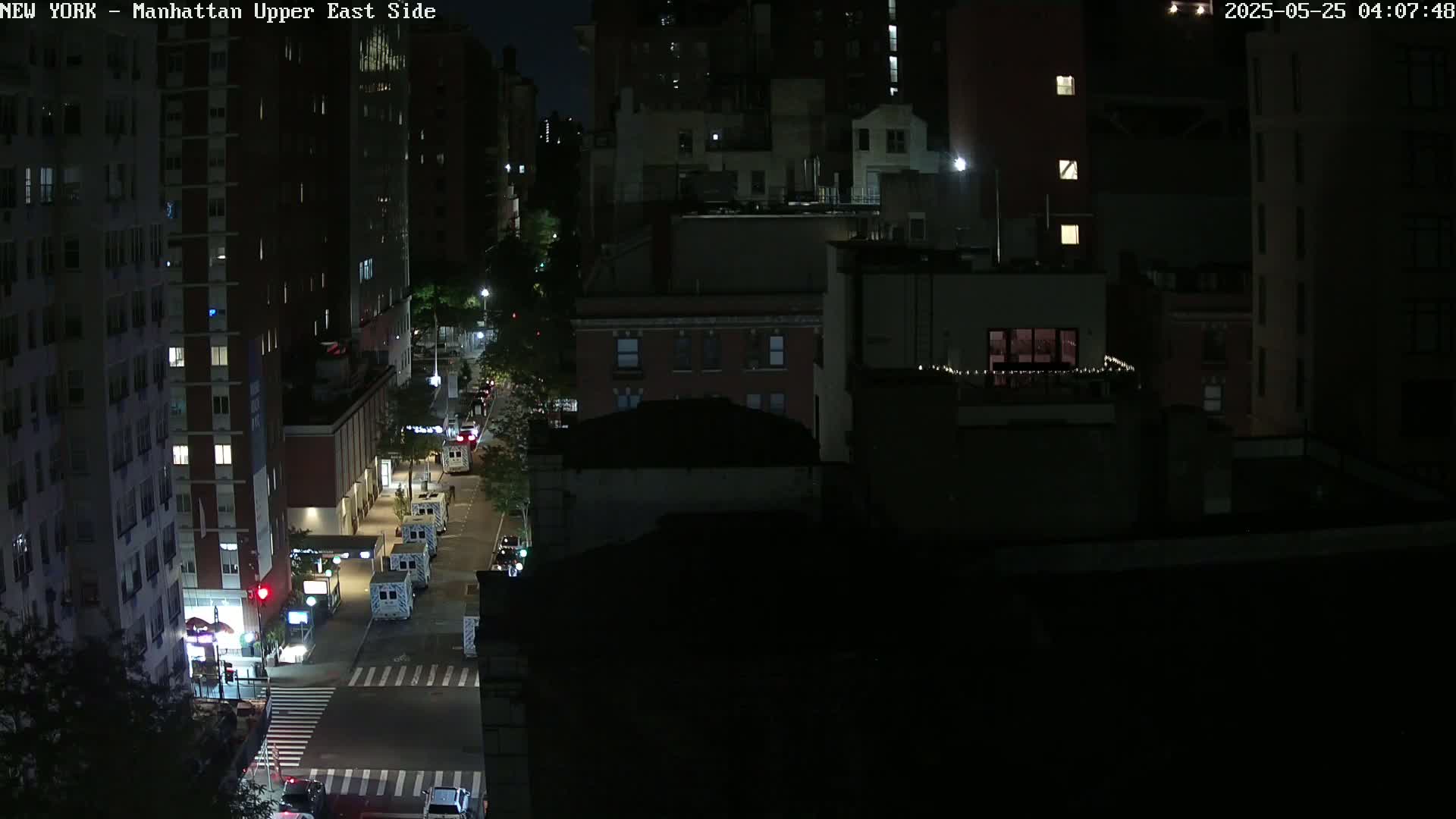 A nighttime, high-angle view of a city street with several vehicles parked along the side, illuminated by streetlights and building lights.