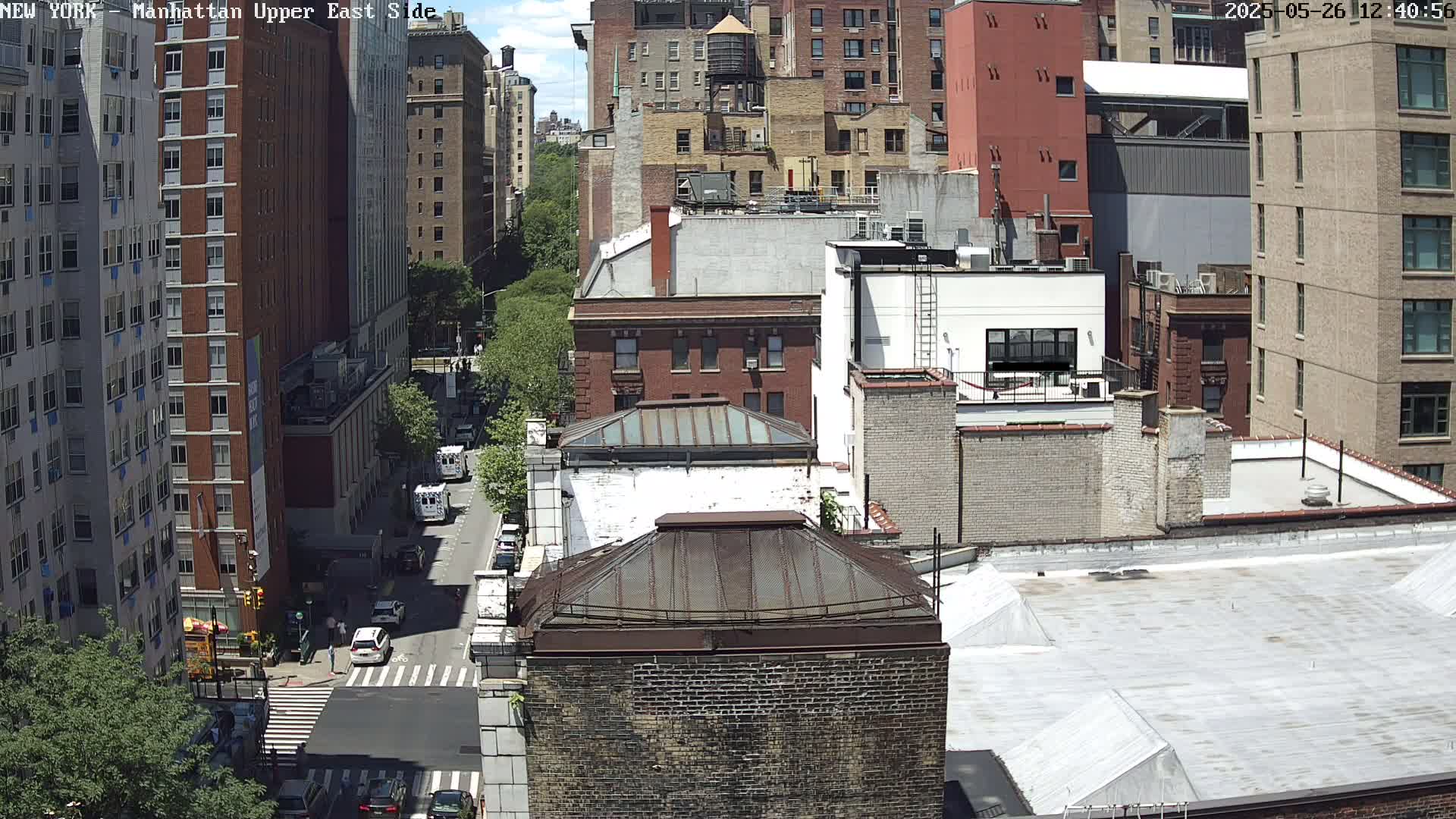 A high-angle view of city buildings on a sunny day, showing a street with cars and pedestrians.