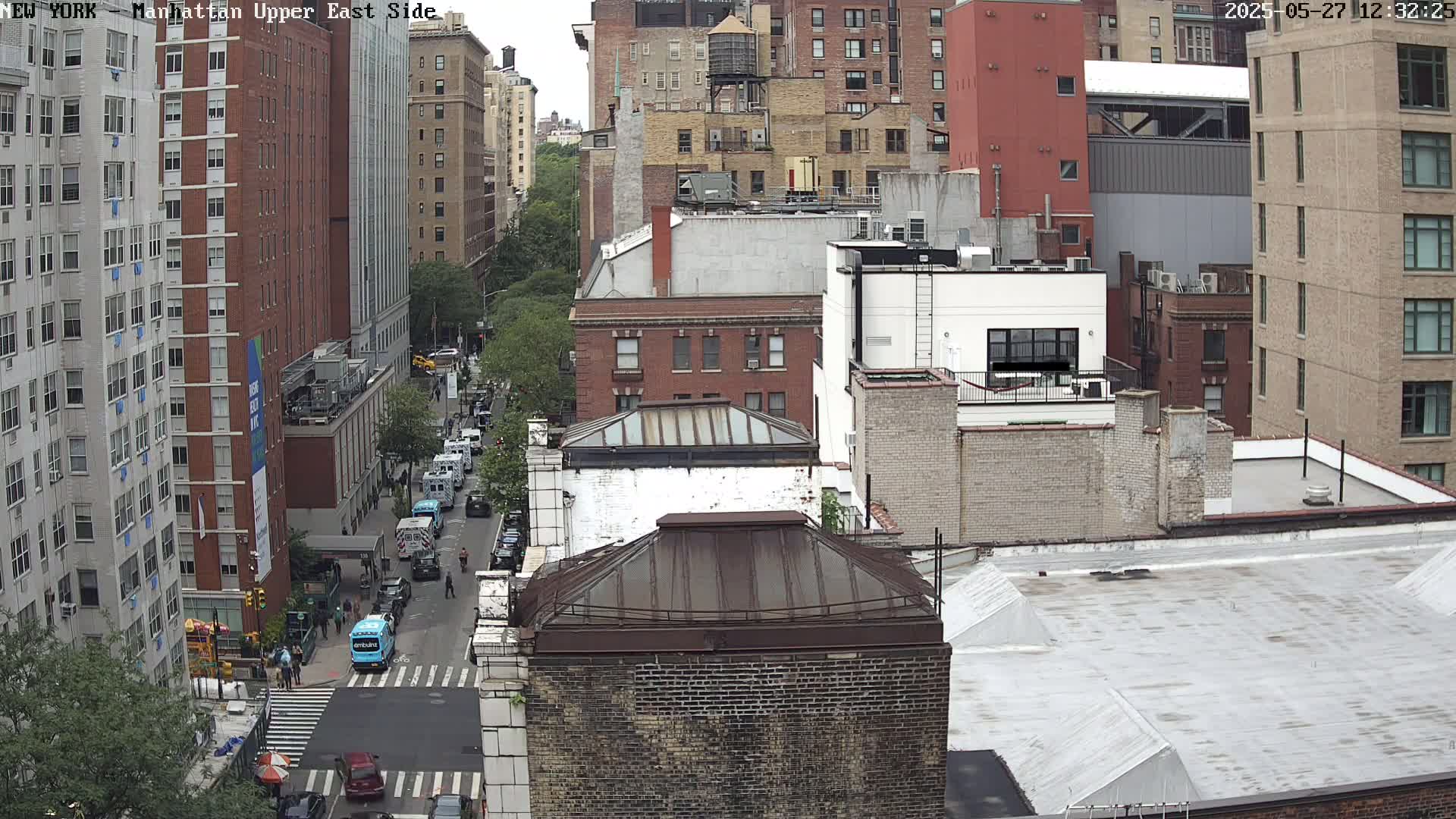 An aerial view of city buildings on a cloudy day, showing a street with several vehicles, including ambulances.