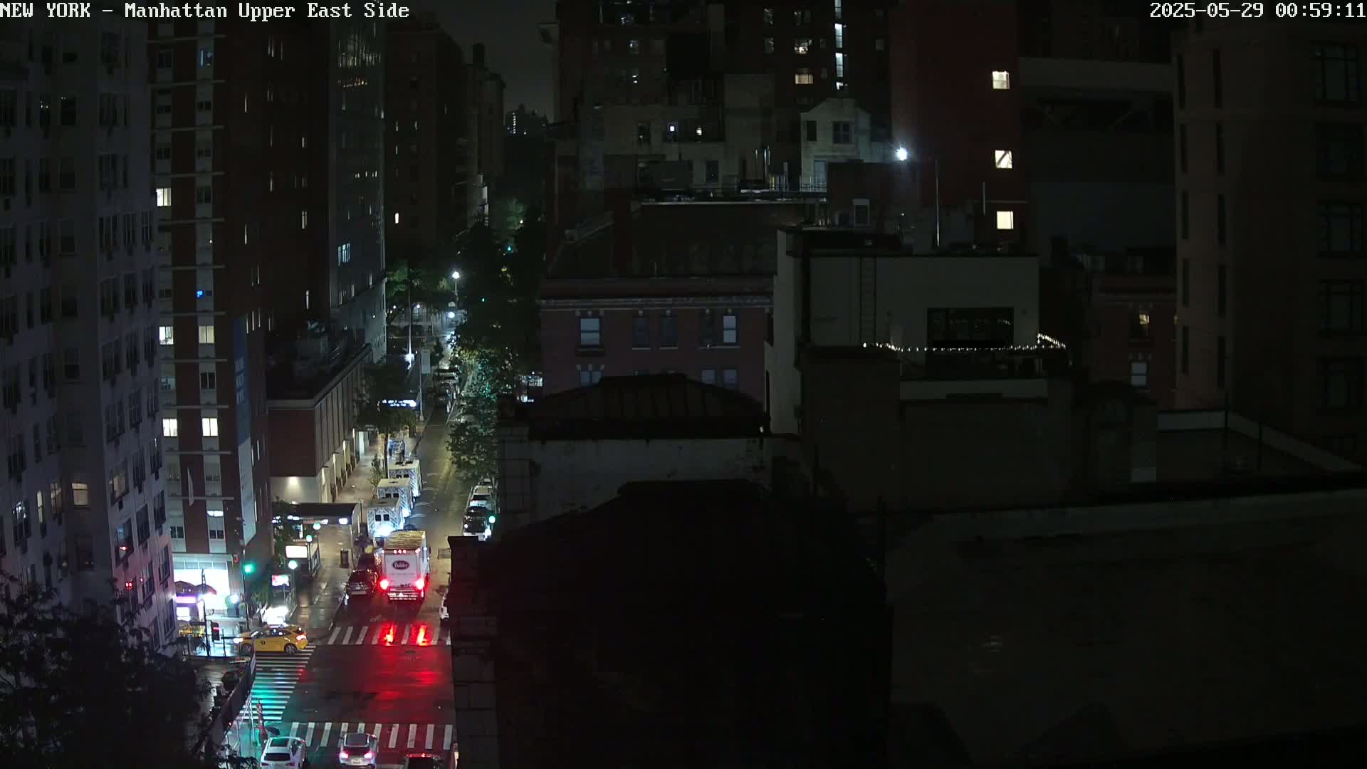 A nighttime, high-angle view of a city street with several buildings and a few cars visible under artificial light.