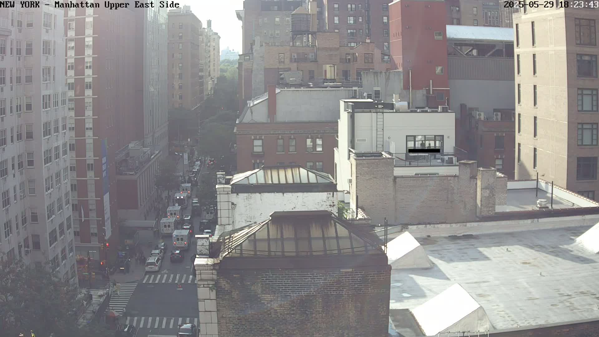 A hazy, sunny day view of a city street with several multi-story buildings, showing traffic on a city street below.