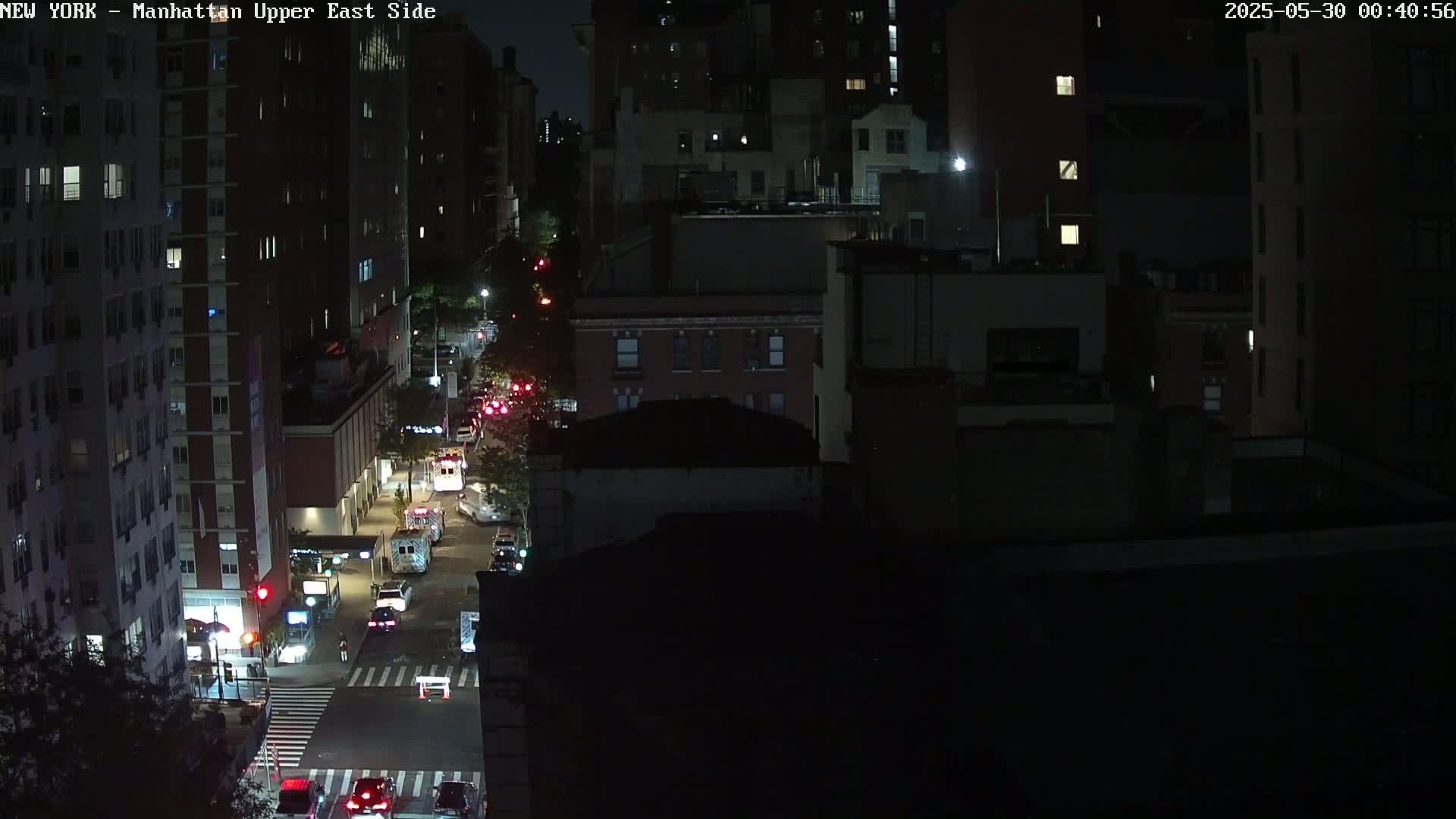 A nighttime, high-angle view of a city street with several vehicles and buildings under dark, clear skies.
