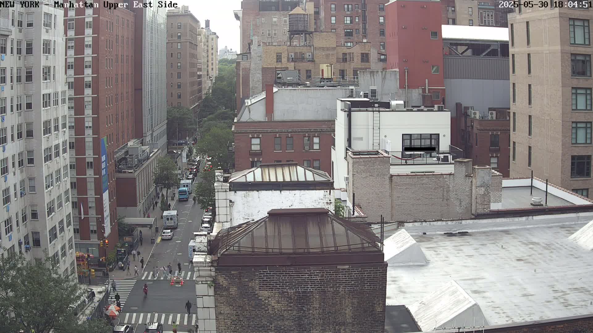 A high-angle, long shot of a city street scene on an overcast day, showing several multi-story brick buildings and vehicles on a street below.