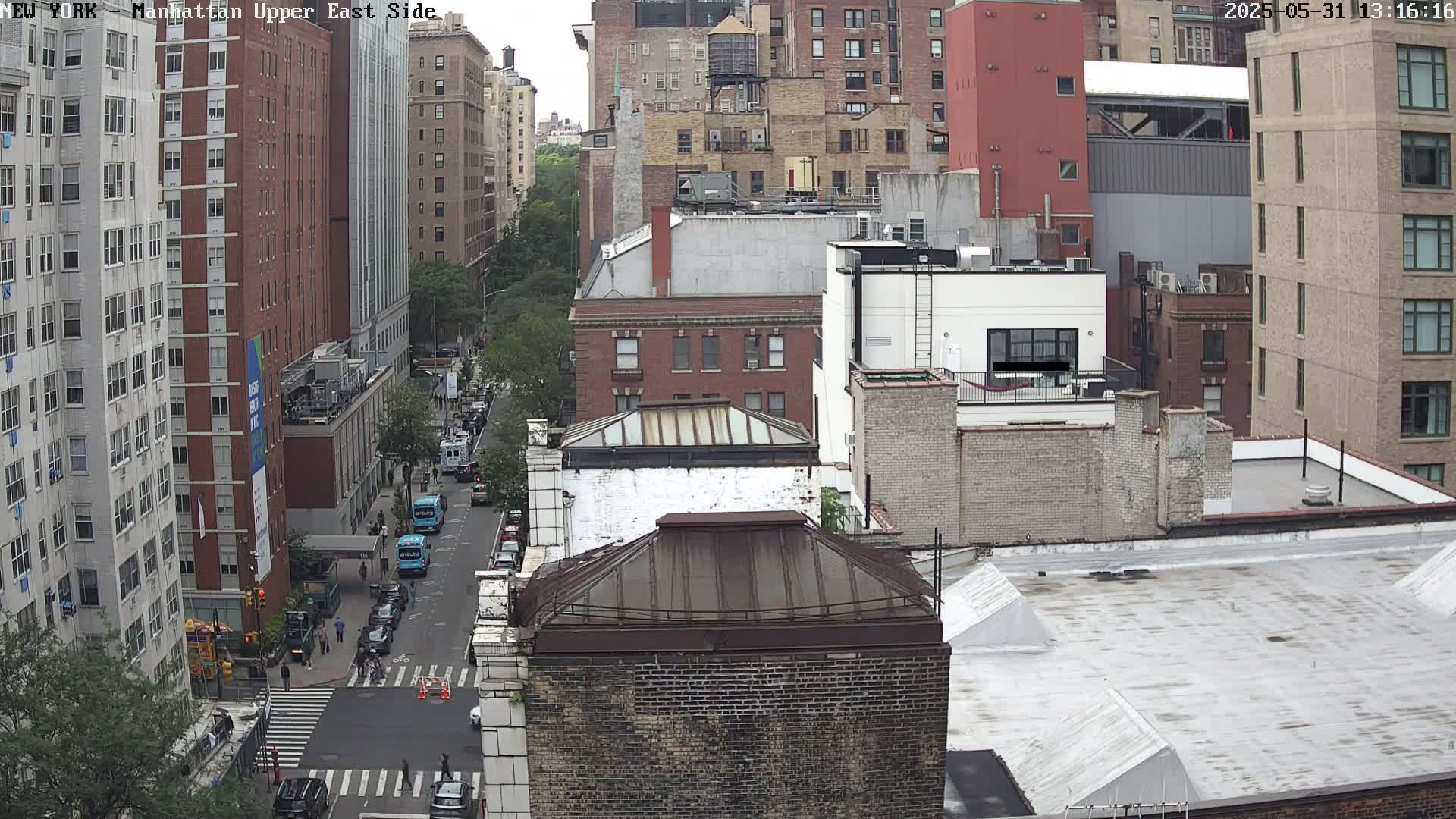 A high-angle view of a city street with several multi-story buildings on a partly cloudy day.