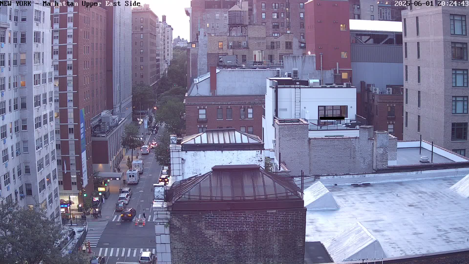 An aerial view of a city street at dusk shows several multi-story buildings and cars on a street below.