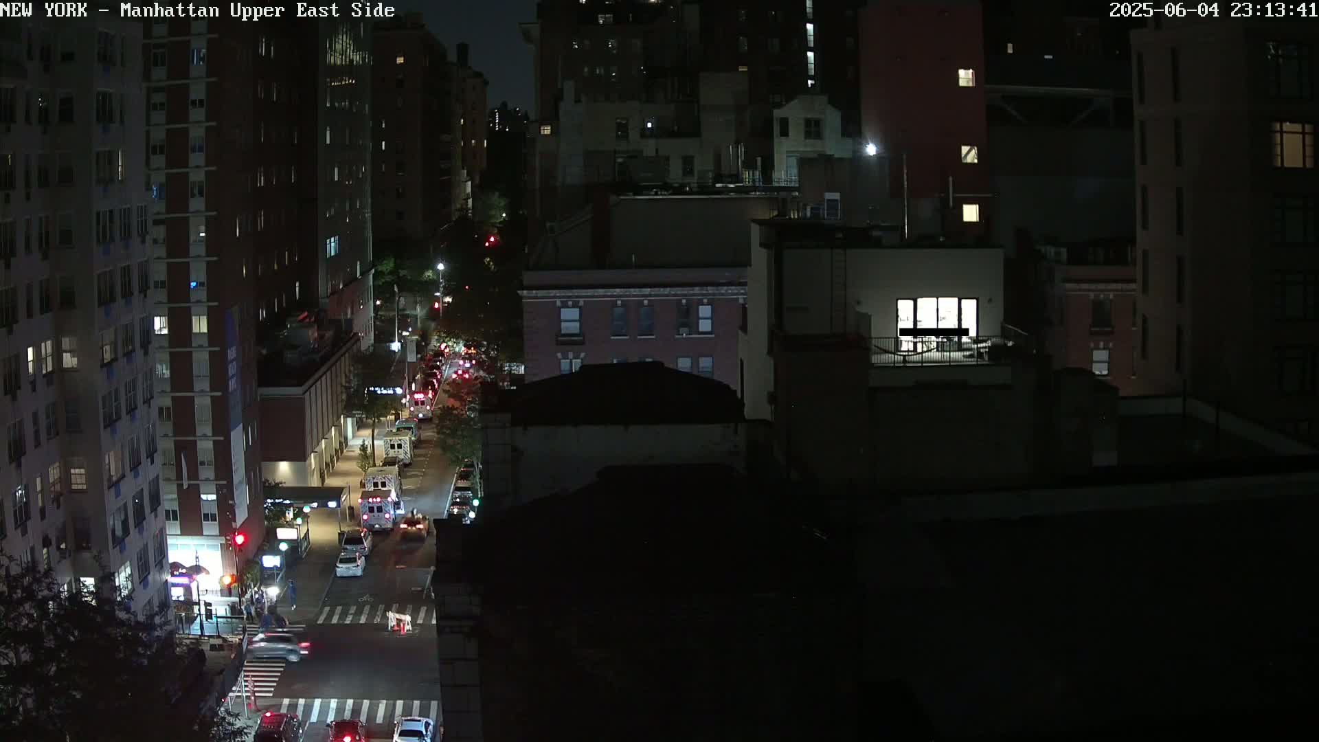A nighttime aerial view of a city street with cars and buildings, under dark conditions.