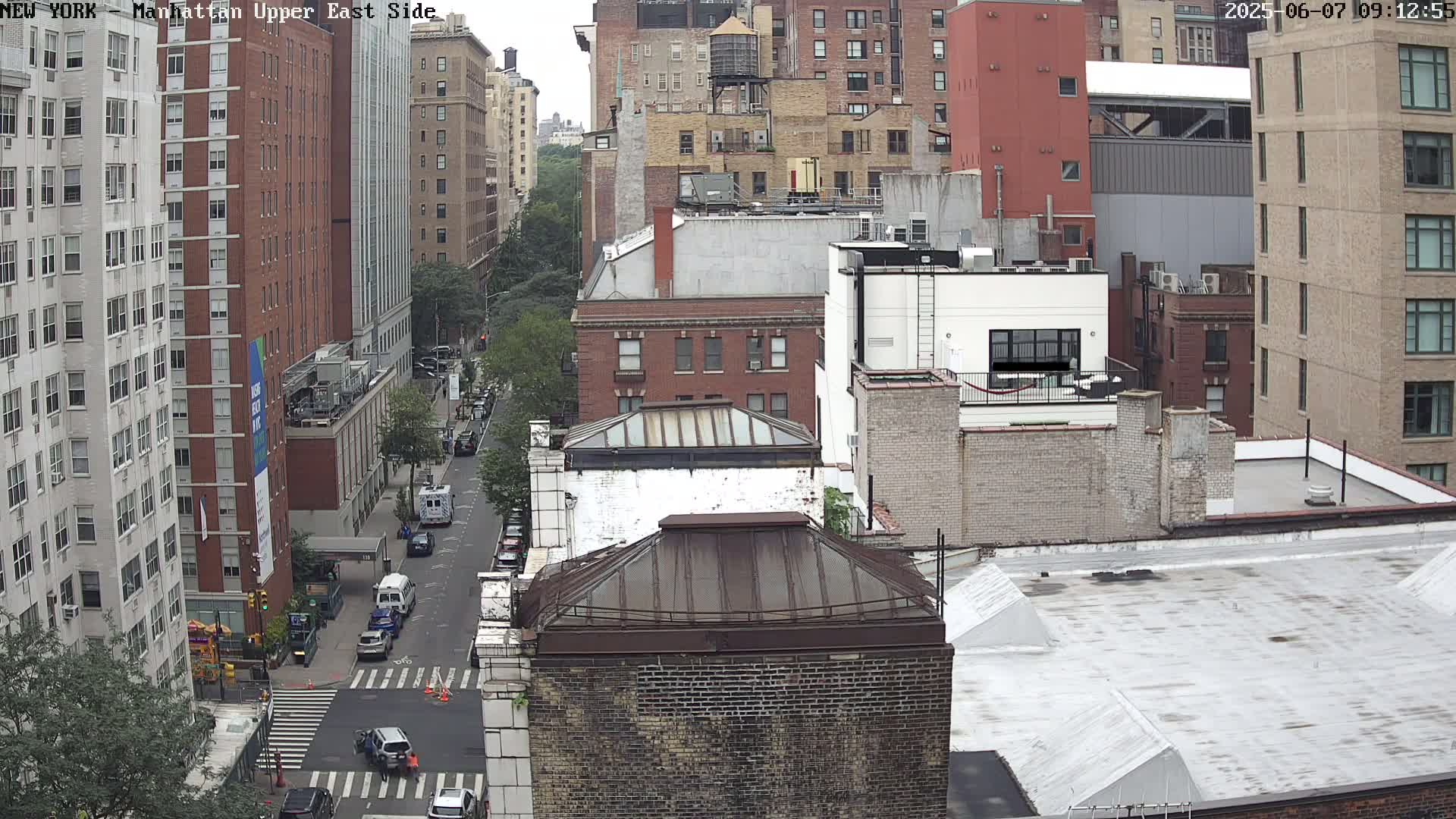 A high-angle, long shot of a city street with several multi-story buildings on a cloudy day.