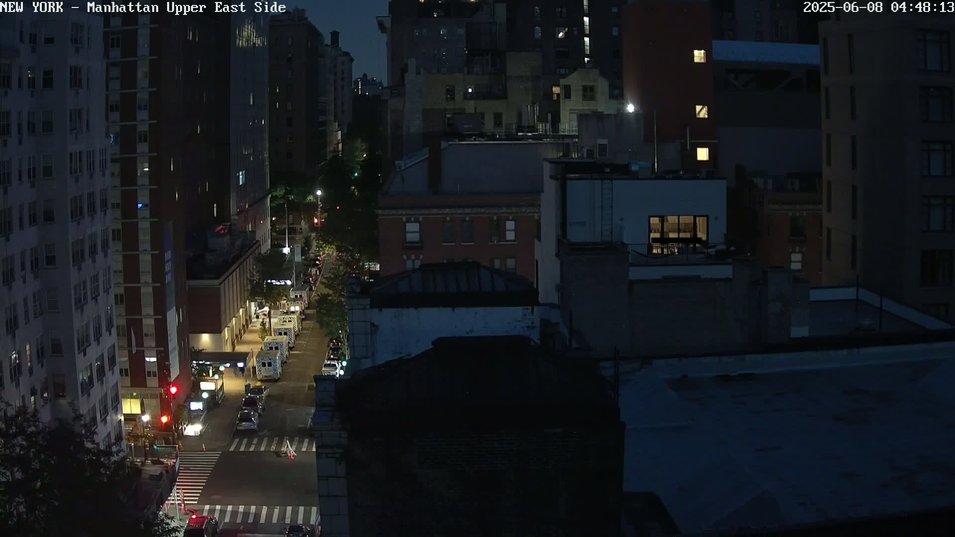 A nighttime, high-angle view of a city street with several buildings and sparse vehicle traffic under dark skies.