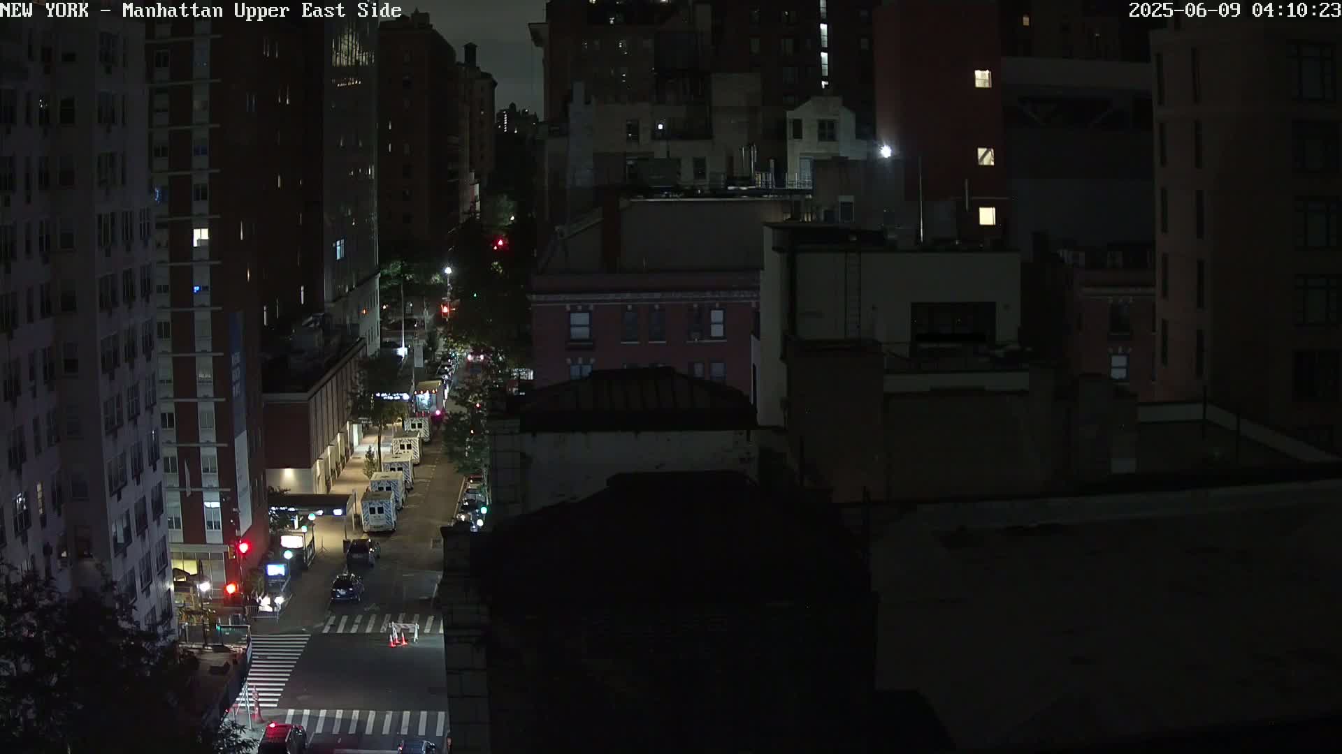 A nighttime aerial view shows a city street with several vehicles, and dark city buildings under a clear, dark sky.