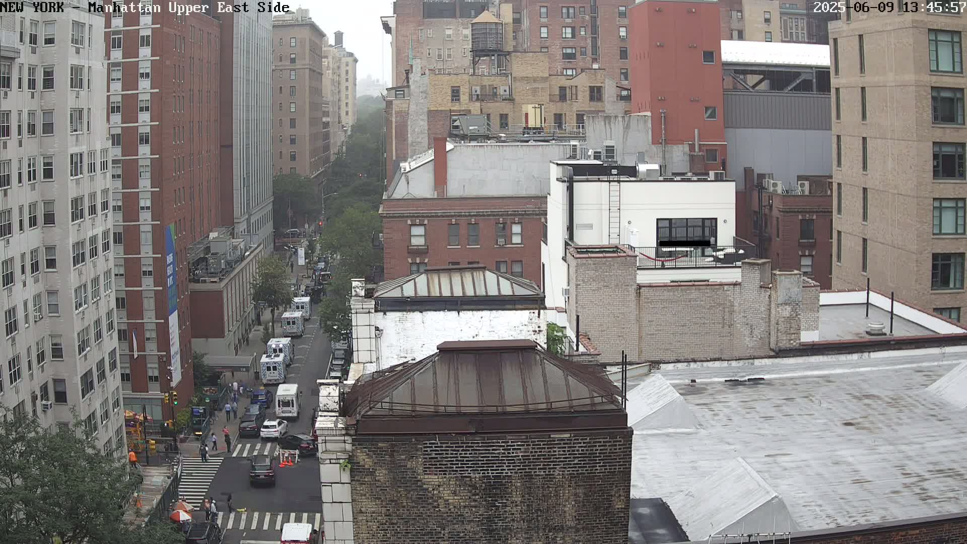A high-angle view of a city street scene on an overcast day, showing several city blocks with tall buildings and vehicles on the street below.