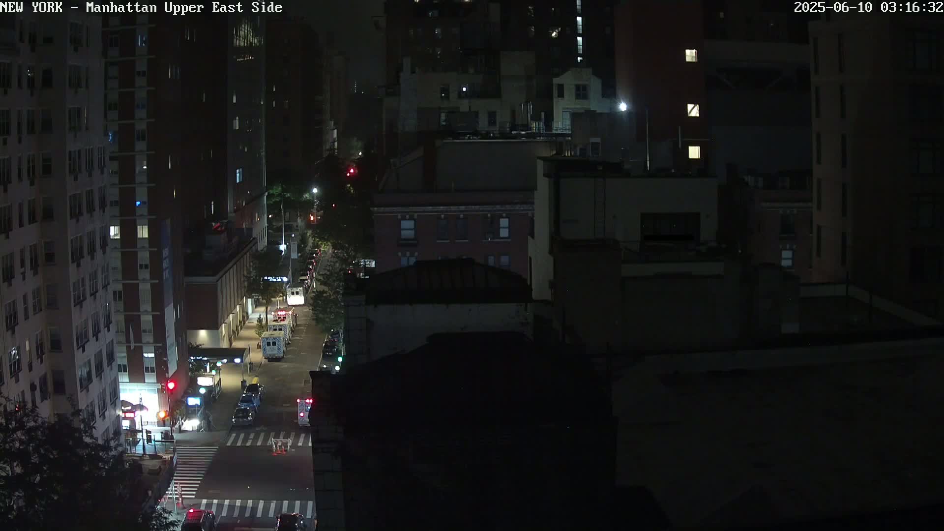 A nighttime, high-angle view of a city street with sparsely moving vehicles and several multi-story buildings.