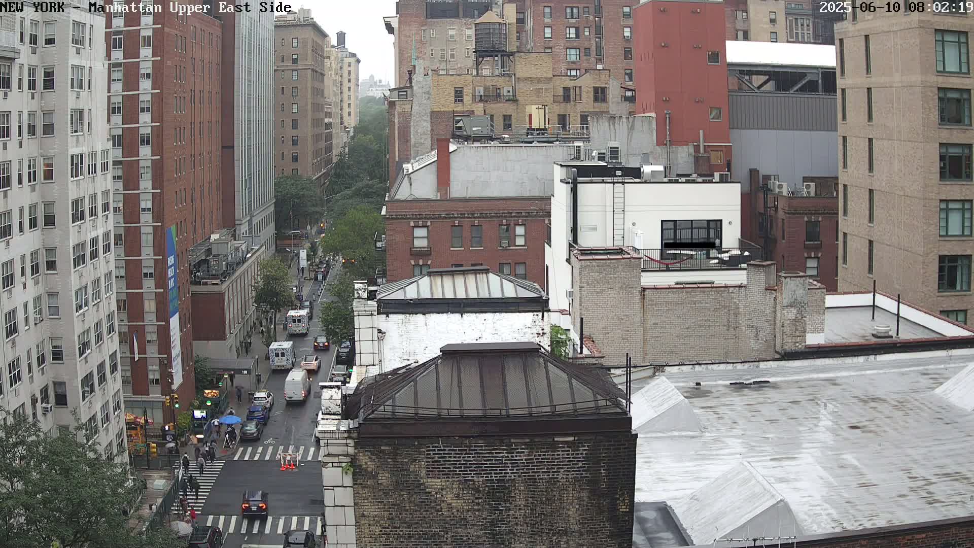A high-angle view of a city street scene on an overcast day, showing multiple brick buildings and vehicles on a street below.
