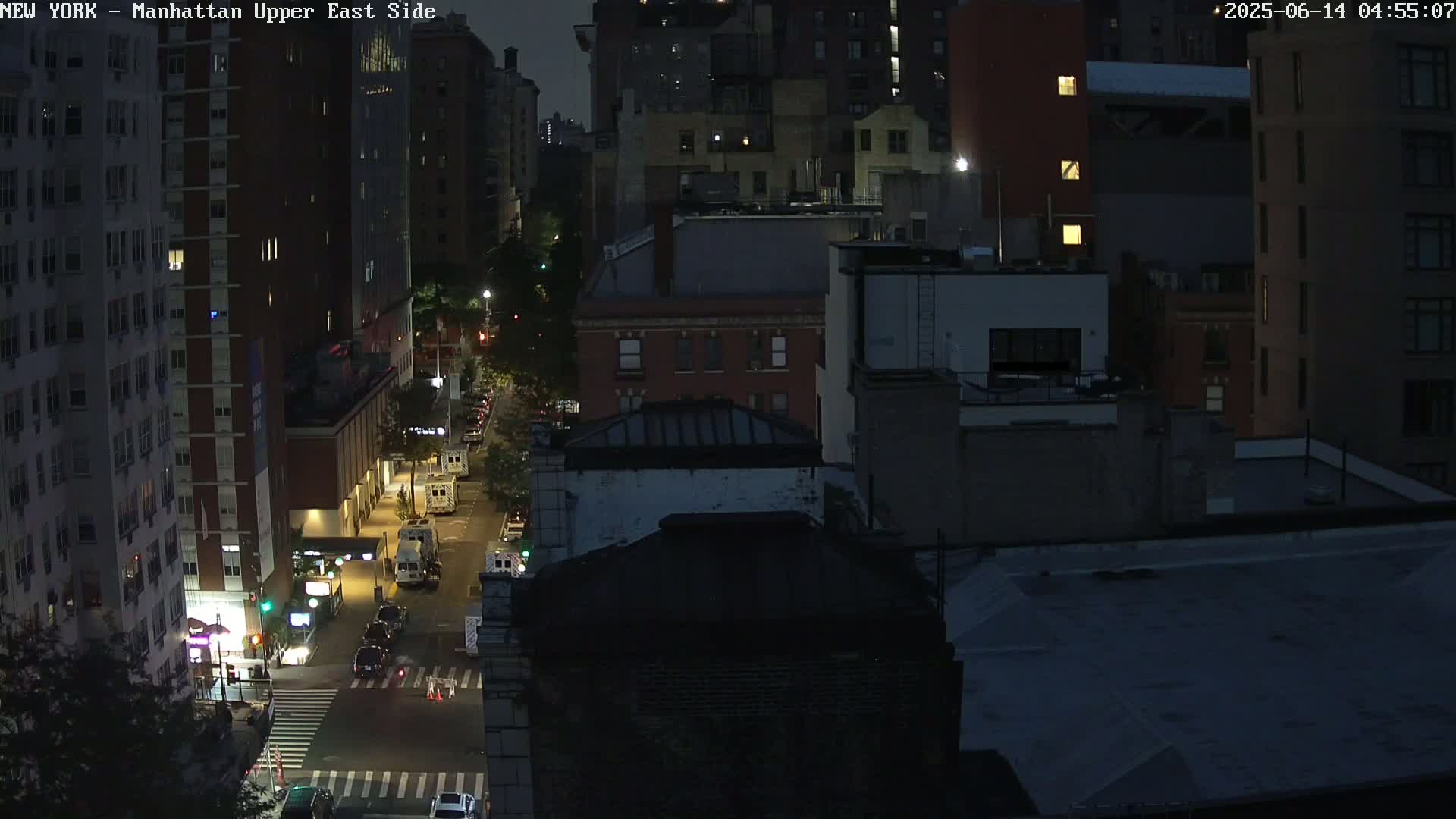 A nighttime aerial view of city streets and buildings, with some cars visible on the roads.