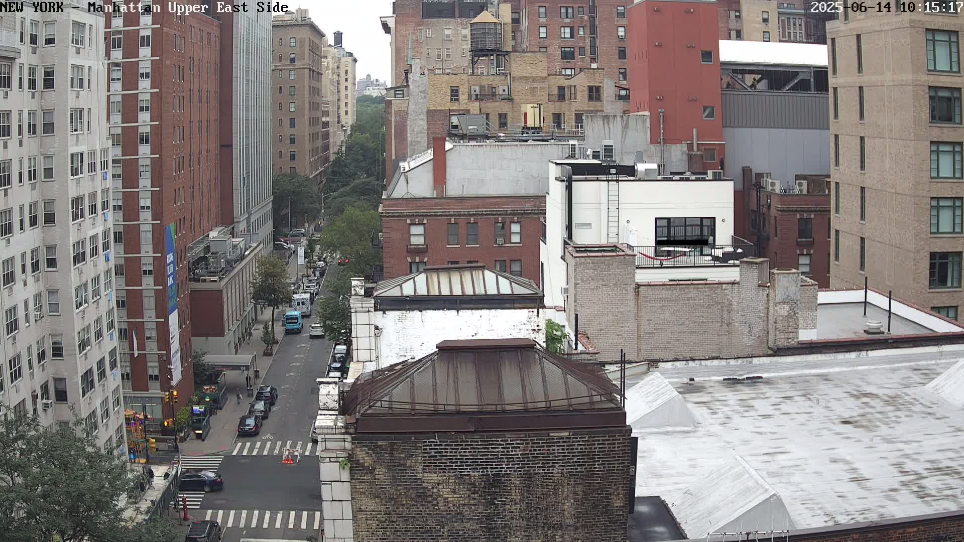 A high-angle view of a city street scene on an overcast day, showing several multi-story brick buildings, a street with cars, and a crosswalk.