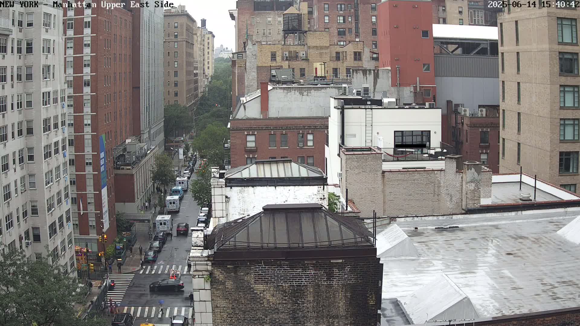 A high-angle view of a city street scene on an overcast day, showing several multi-story brick buildings, a street with cars, and a crosswalk.