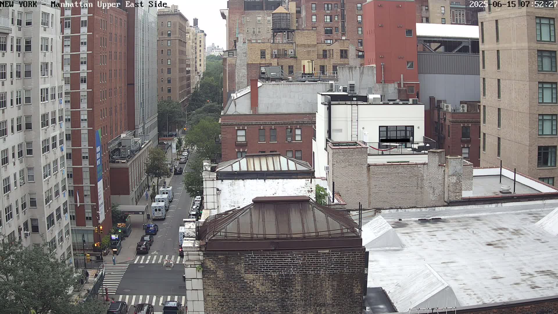 A high-angle view of a city street scene on an overcast day, showing several multi-story brick buildings and vehicles on the street below.