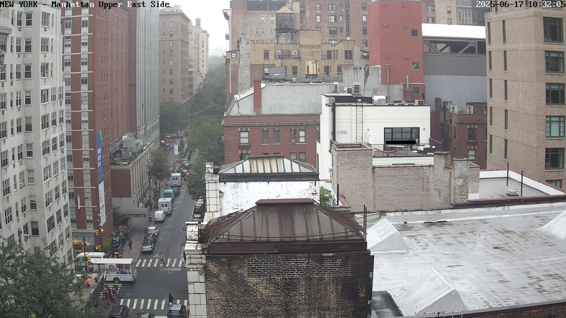 A high-angle view of a city street scene on an overcast day, showing several multi-story buildings and vehicles on a street below.