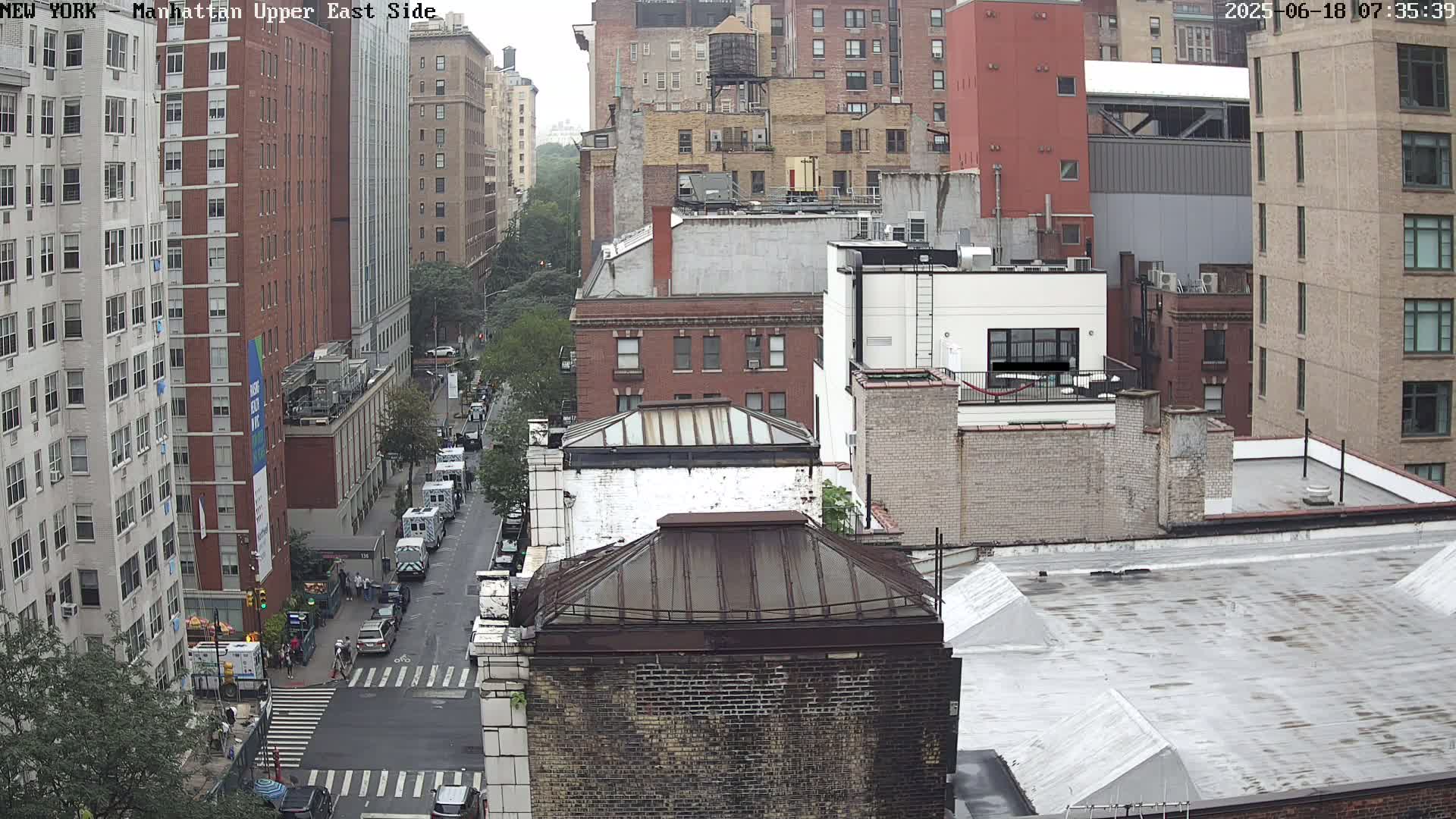 A high-angle view of a city street scene on a cloudy day, showing several multi-story buildings and vehicles on a street below.